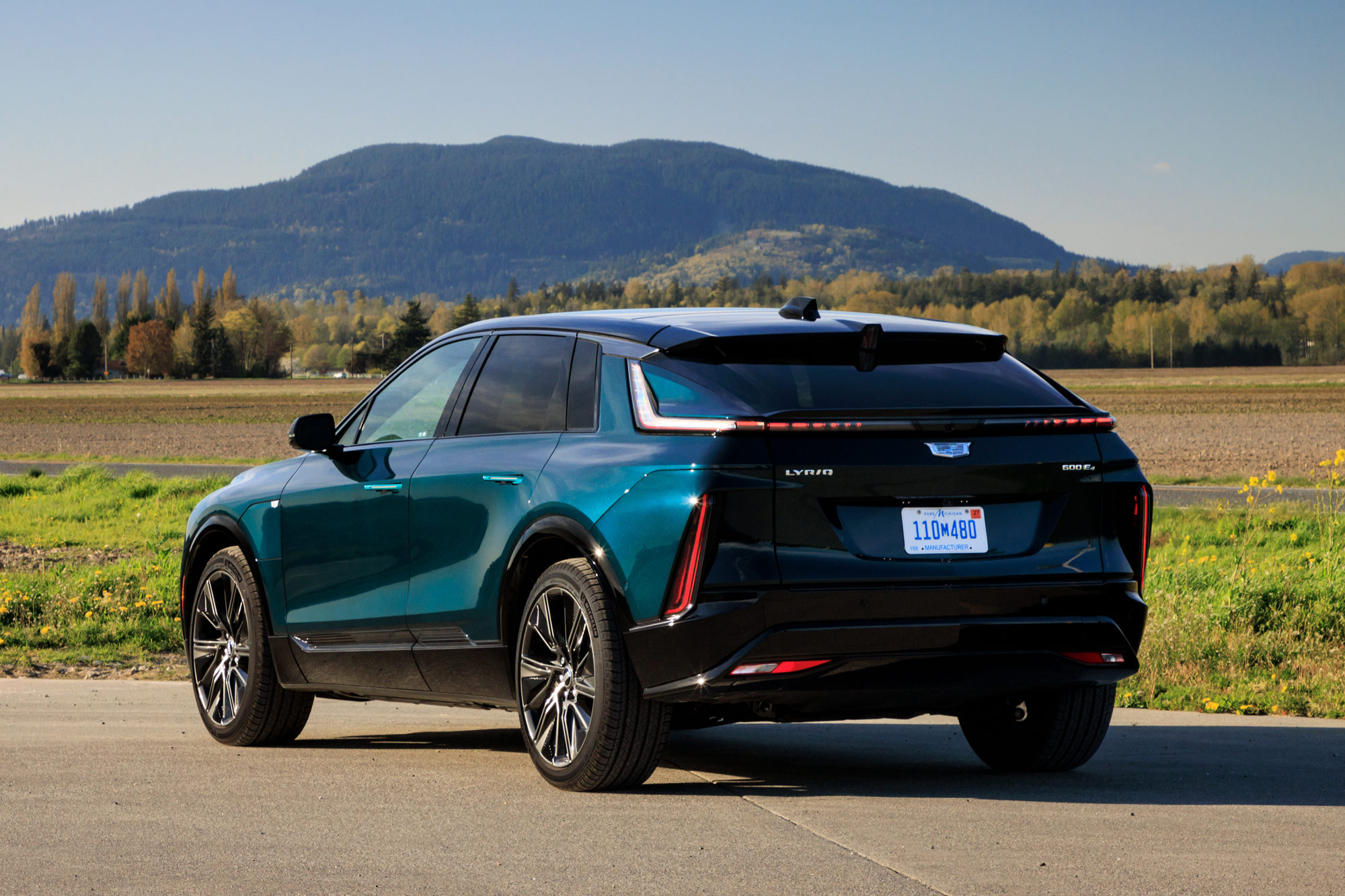 Rear-quarter of a blue-green 2024 Cadillac Lyriq parked with mountains in the background