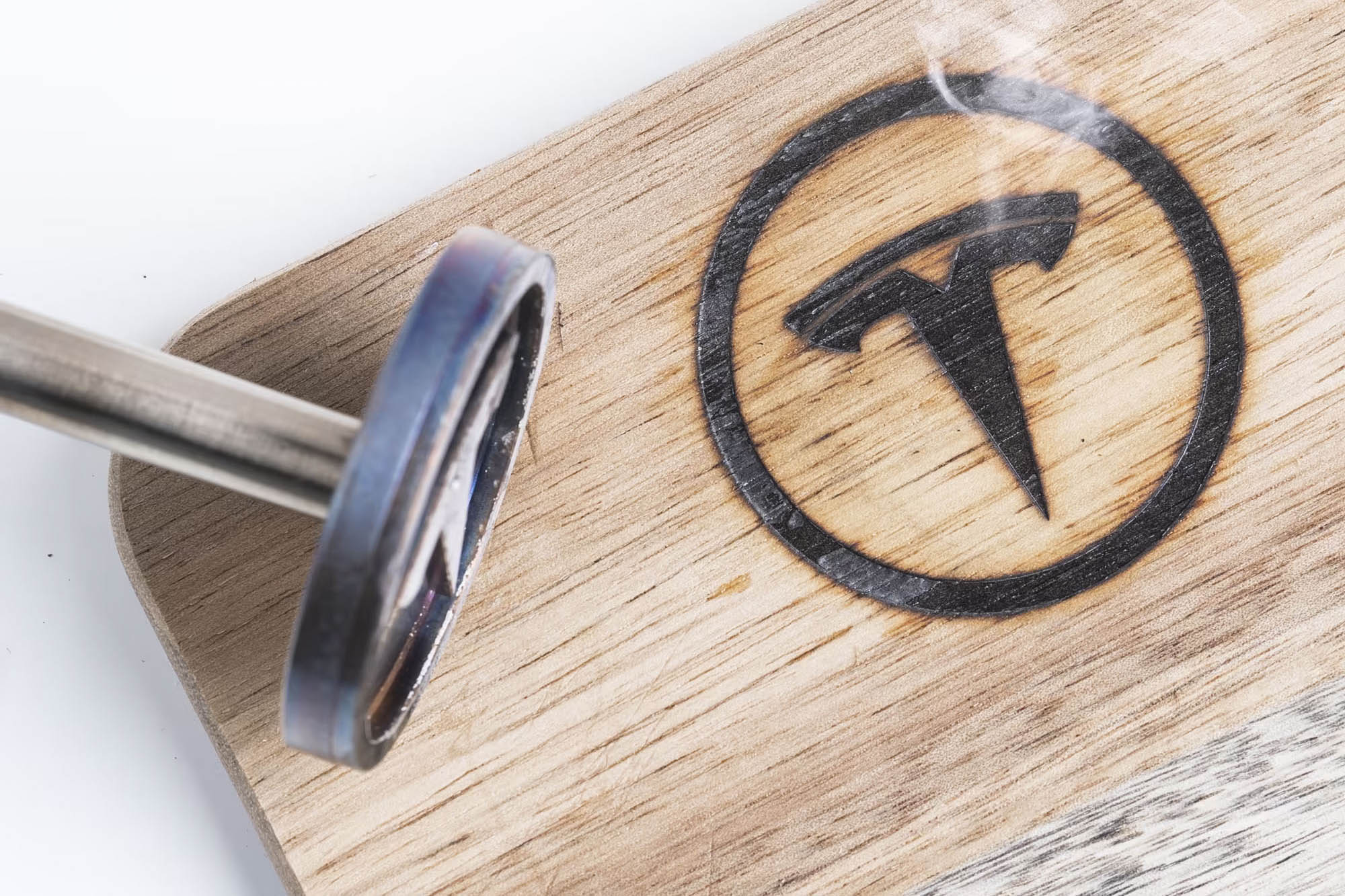 A Tesla branding iron next to a freshly branded piece of wood