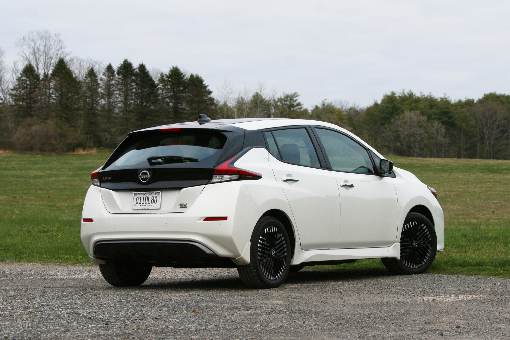 Rear-quarter of a white 2024 Nissan Leaf SV Plus parked next to a field