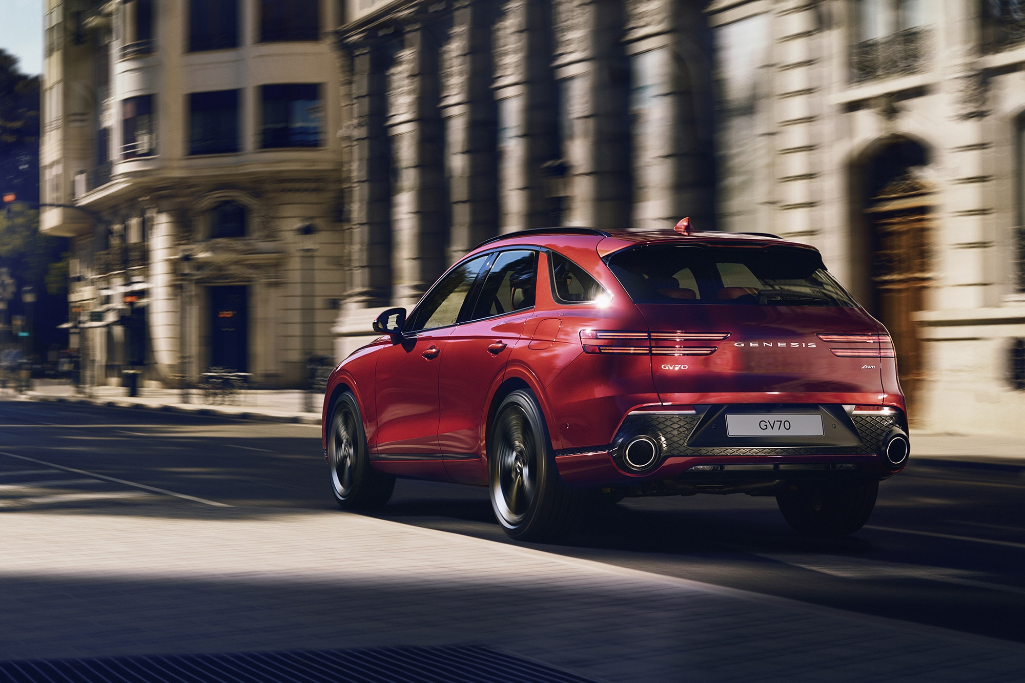 Genesis GV70 in red, driving down an urban road, rear view