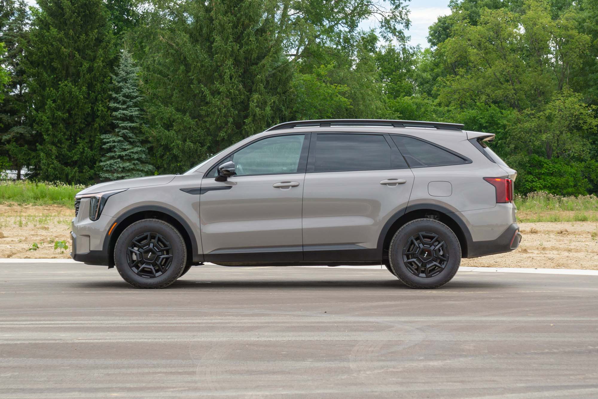 Side view of a Road Rider Brown 2024 Kia Sorento SX Prestige X-Pro parked on a road with trees in the background.