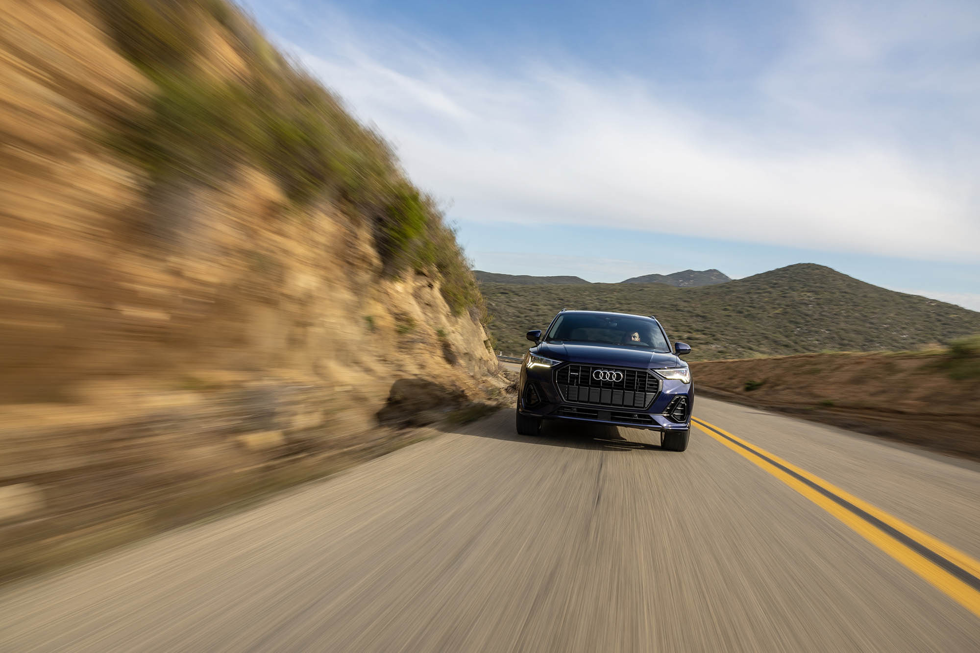 Blue Audi Q3 facing the camera driving on a paved road in the hills.