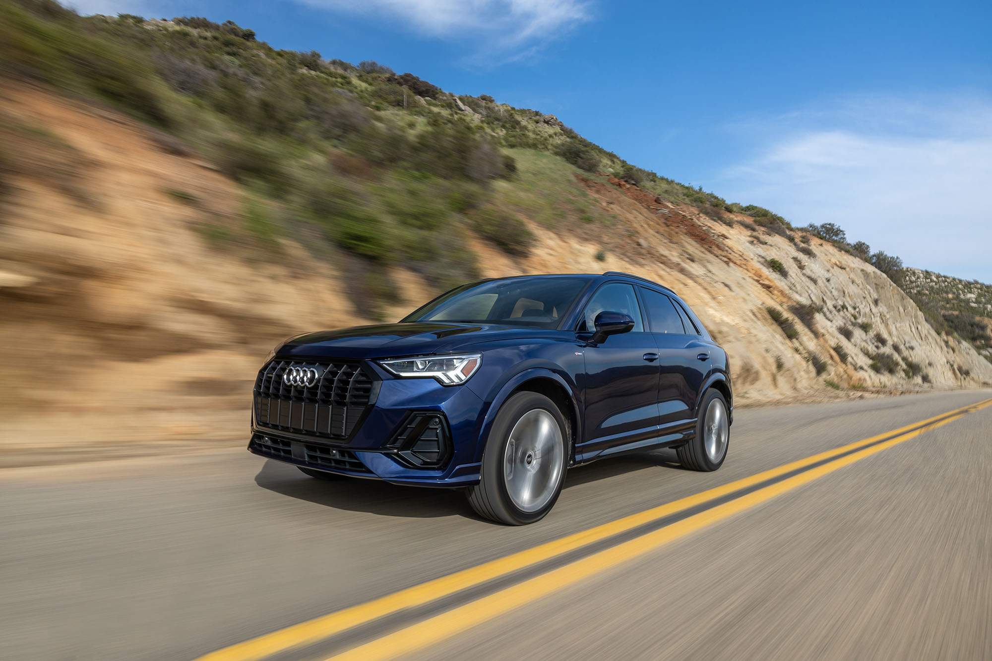 Blue Audi Q3 driving on a paved road in the hills.