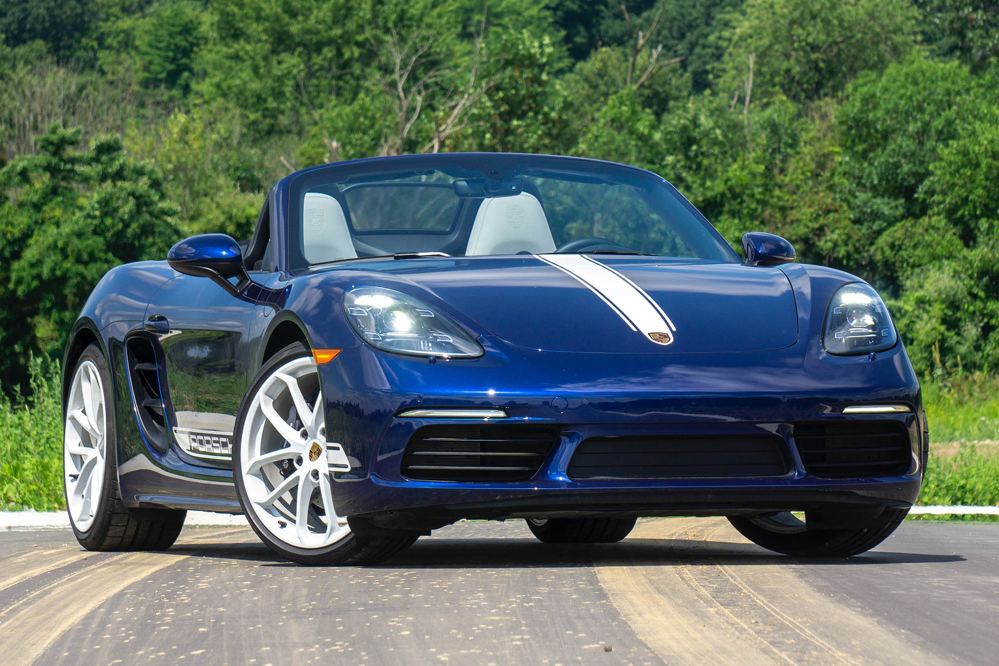 Front-quarter view of a blue 2024 Porsche 718 Boxster Style Edition parked on pavement in front of trees