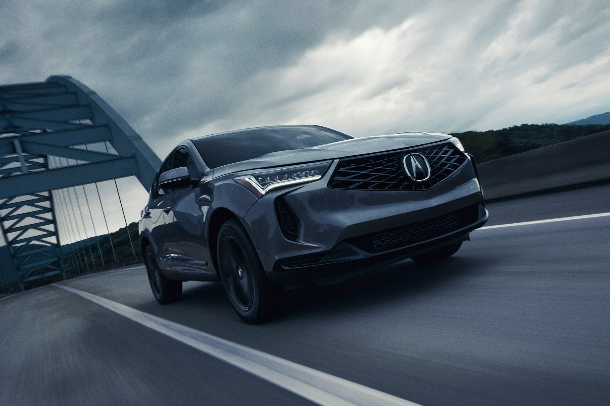 A gray 2025 Acura RDX driving on a highway under a cloudy sky