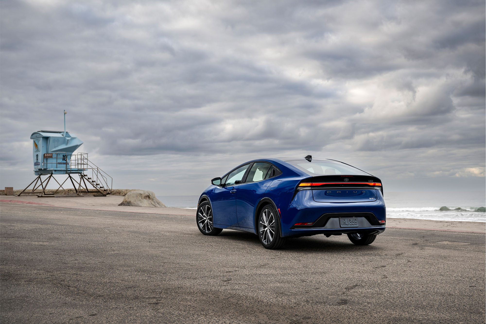 Blue Toyota Prius parked on the beach with a moody sky above.