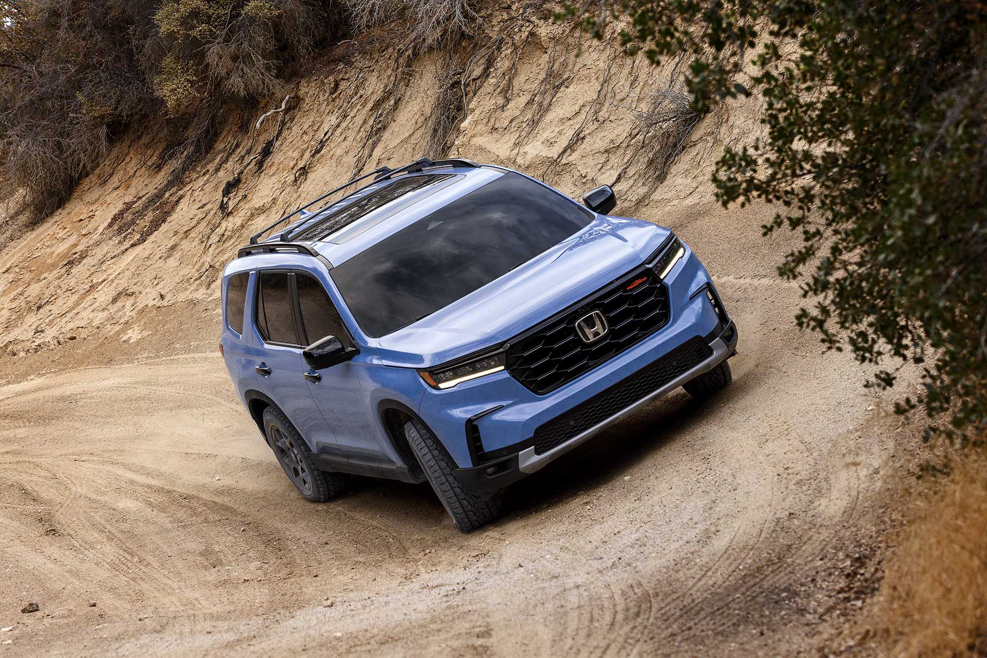 Blue Honda Pilot TrailSport driving on a banked dirt road.