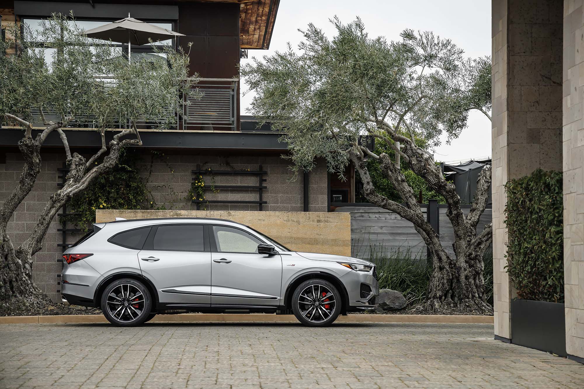 Side view of an Acura MDX in silver parked in front of a residence.