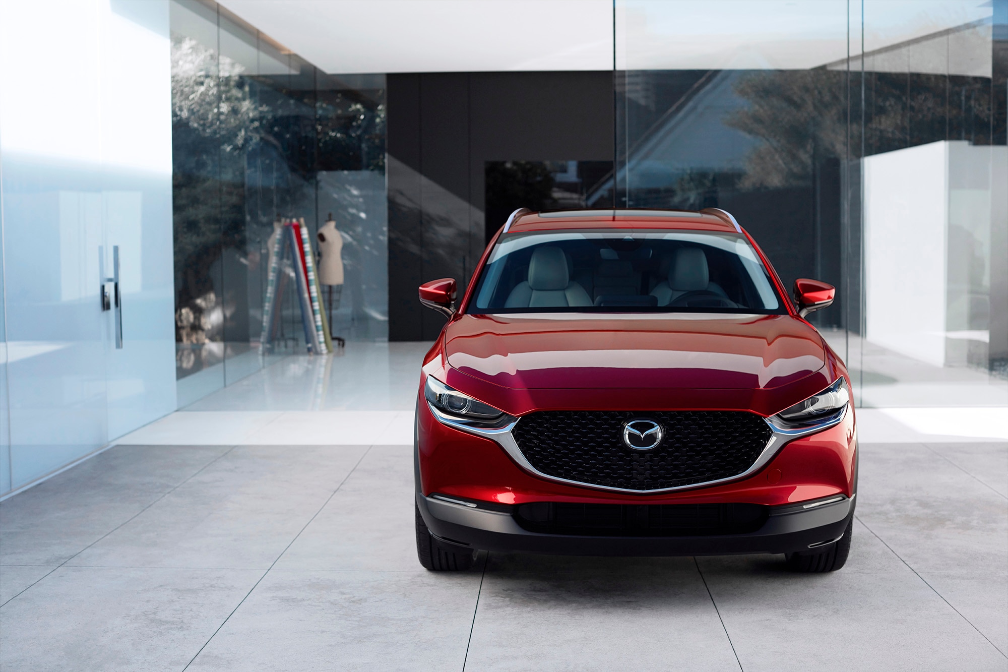 Red Mazda CX-30 parked face first in a building with glass walls.