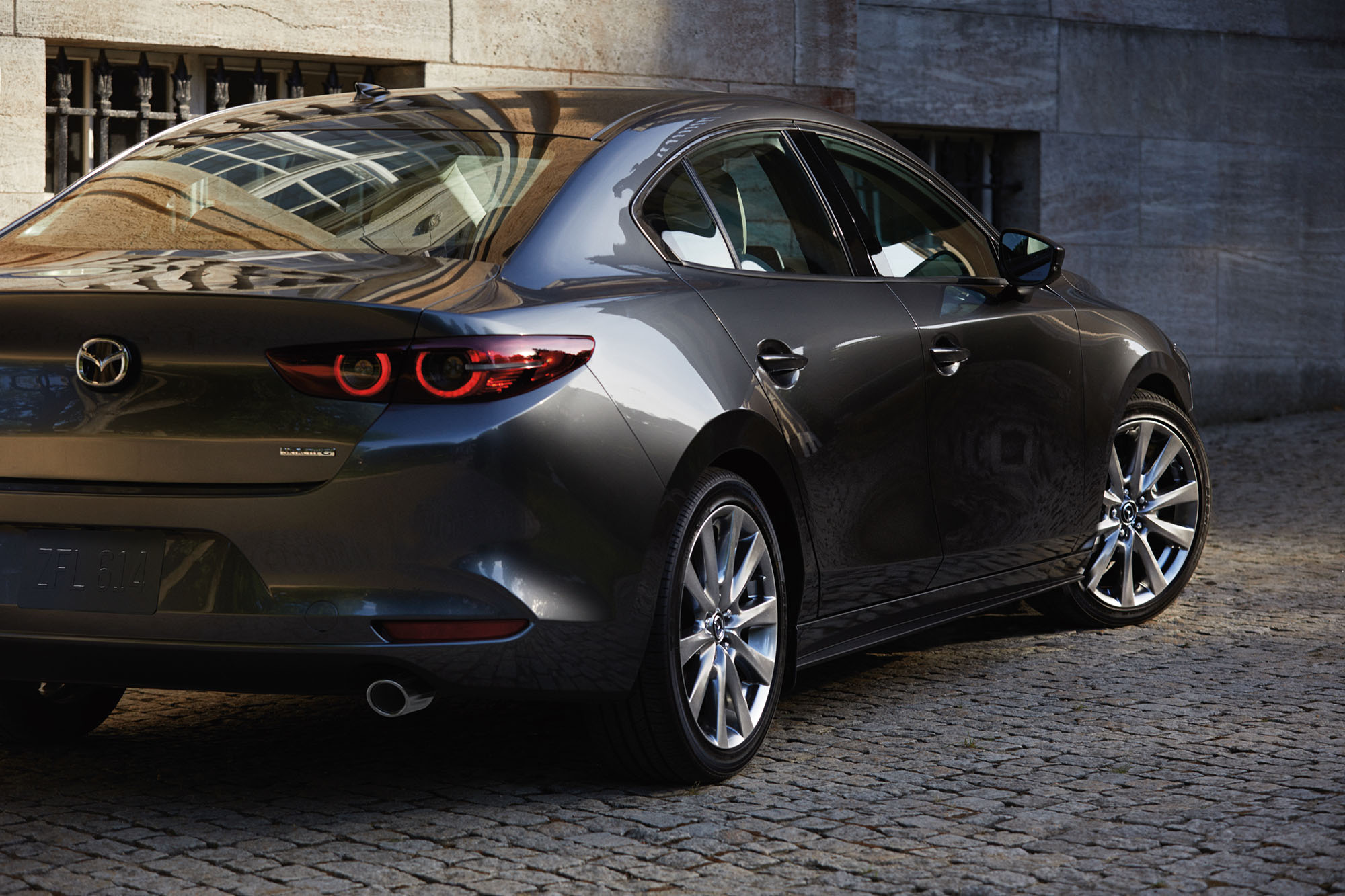 Dark silver Mazda 3 parked on a cobblestone street.