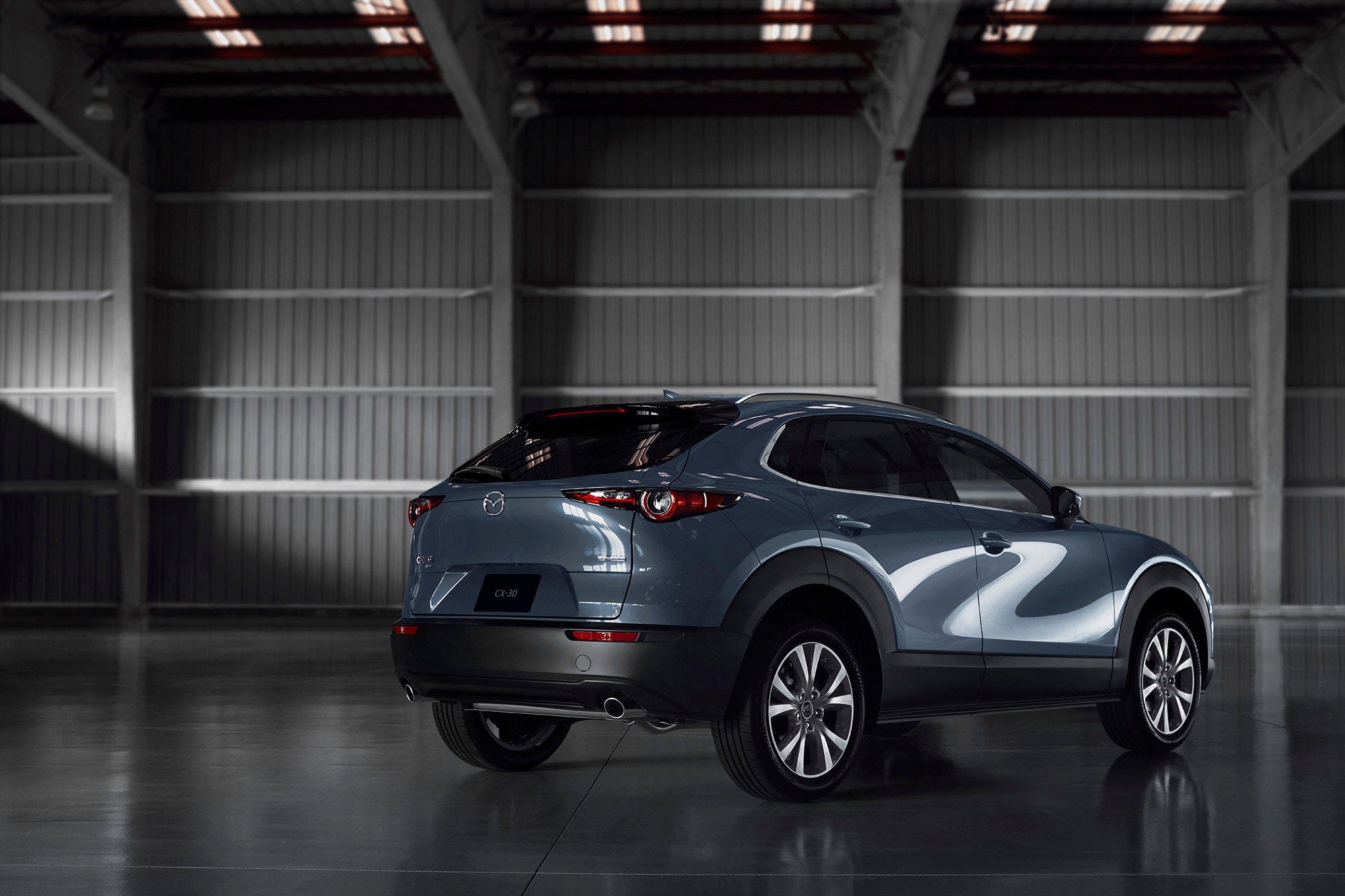 Blue-gray Mazda CX-30 in three-quarter rear view parked in an industrial building.