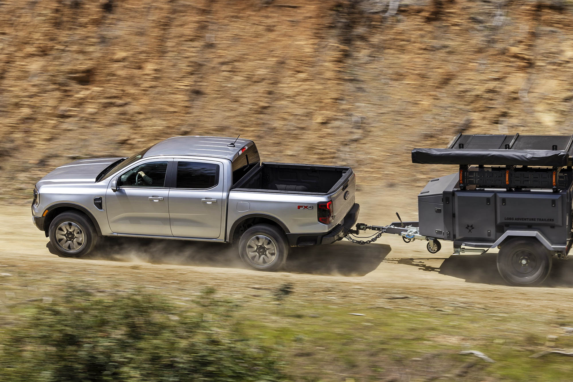 Silver Ford Ranger towing a trailer on a dirt road.