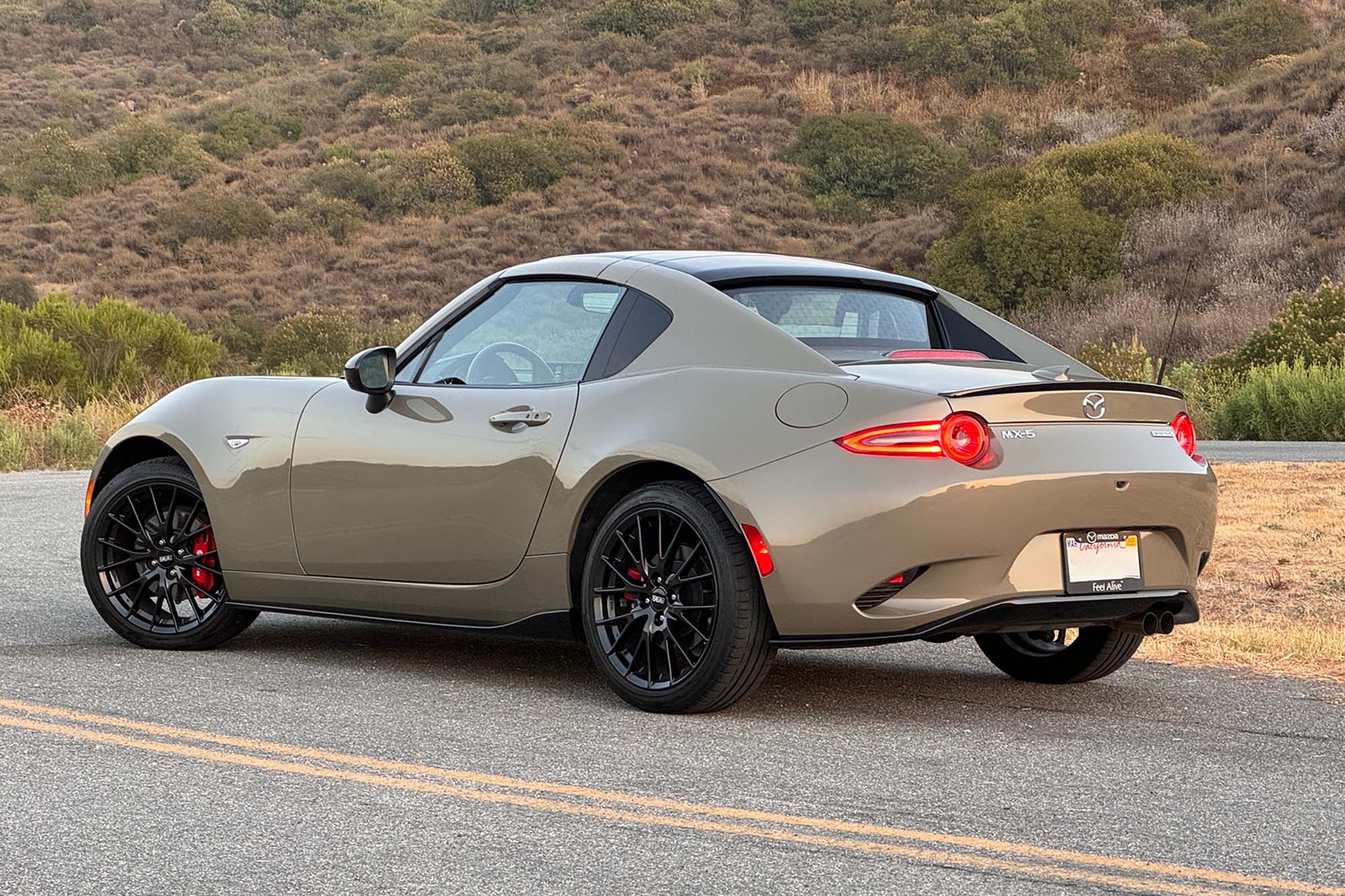 Rear-quarter view of a 2024 Mazda MX-5 Miata RF Club in Zircon Sand, parked on a road at sunset.