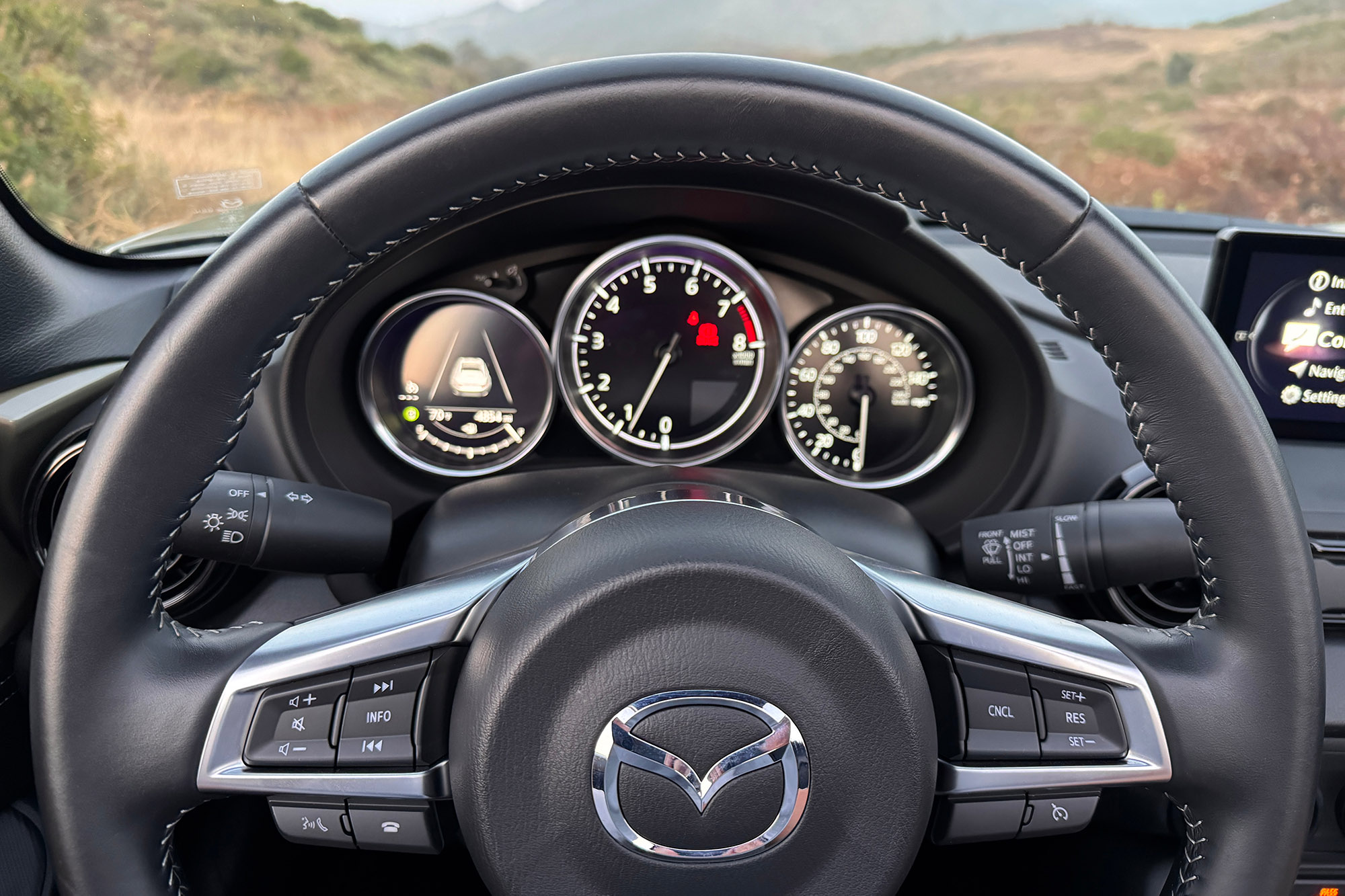 View of a 2024 Mazda MX-5 Miata RF Club interior showing the steering wheel controls and revised gauges.