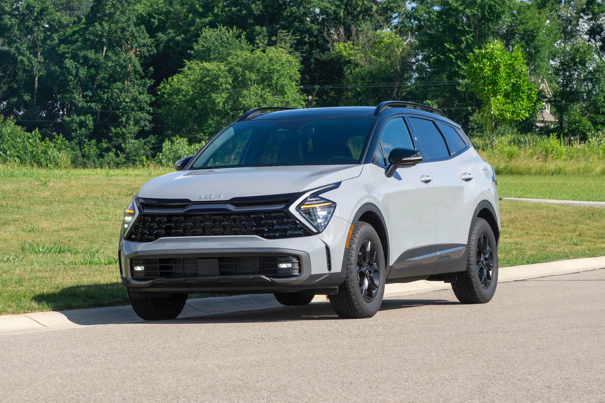 Front-quarter of a Wolf Gray 2024 Kia Sportage X-Pro Prestige parked on a street with trees in the background