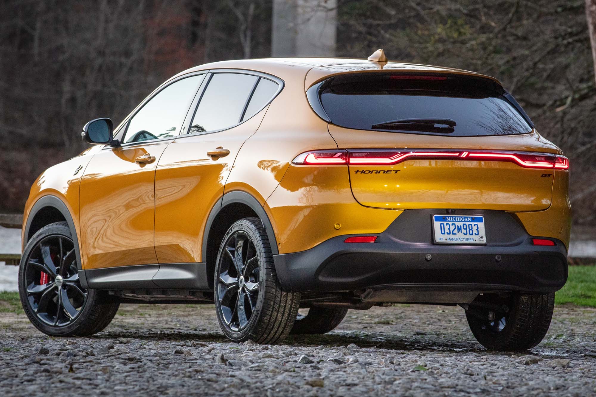 A left-rear view of a yellow 2023 Dodge Hornet parked in front of trees and water