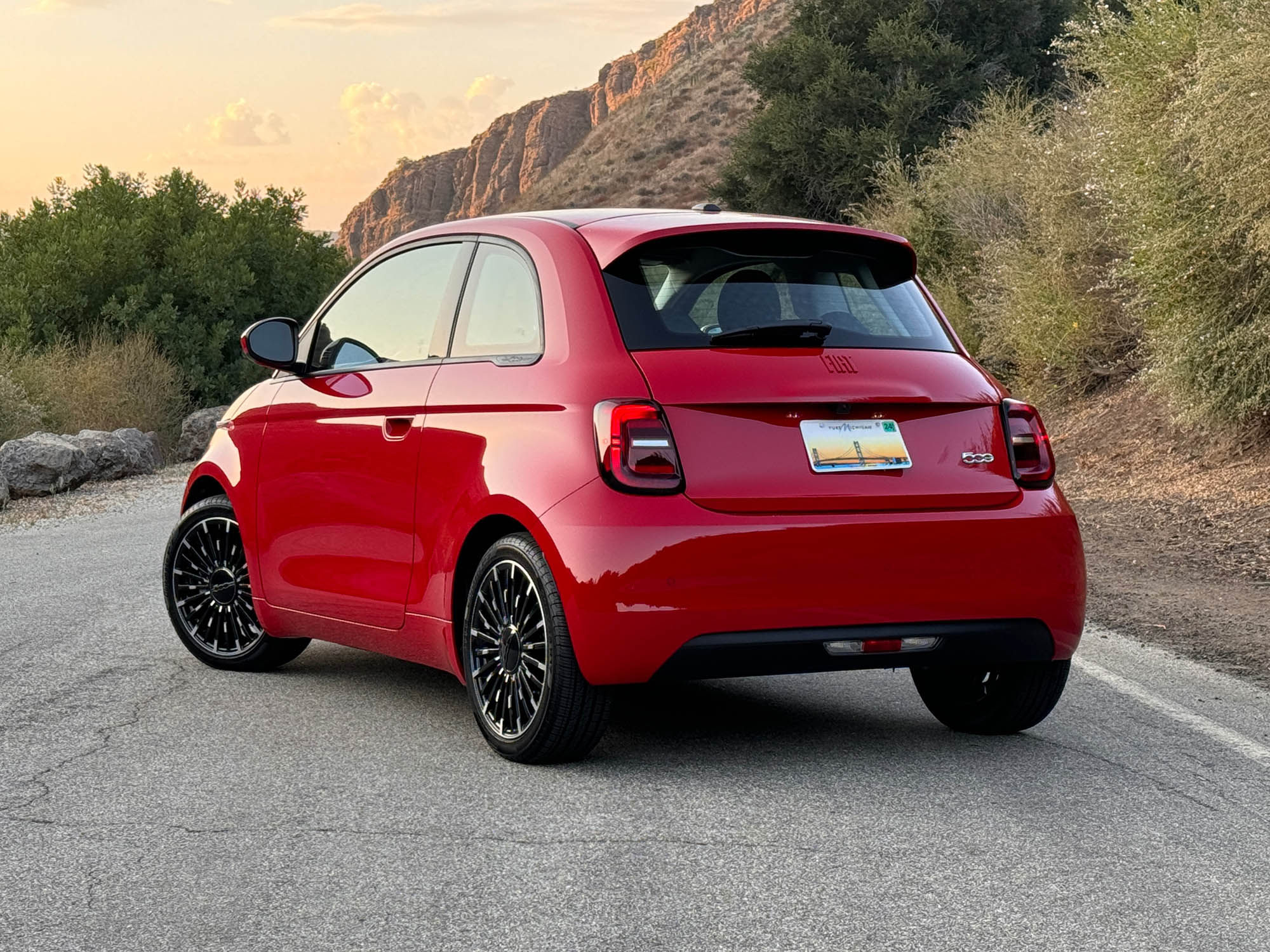 2024 Fiat 500e in red parked on a road at sunset, rear view