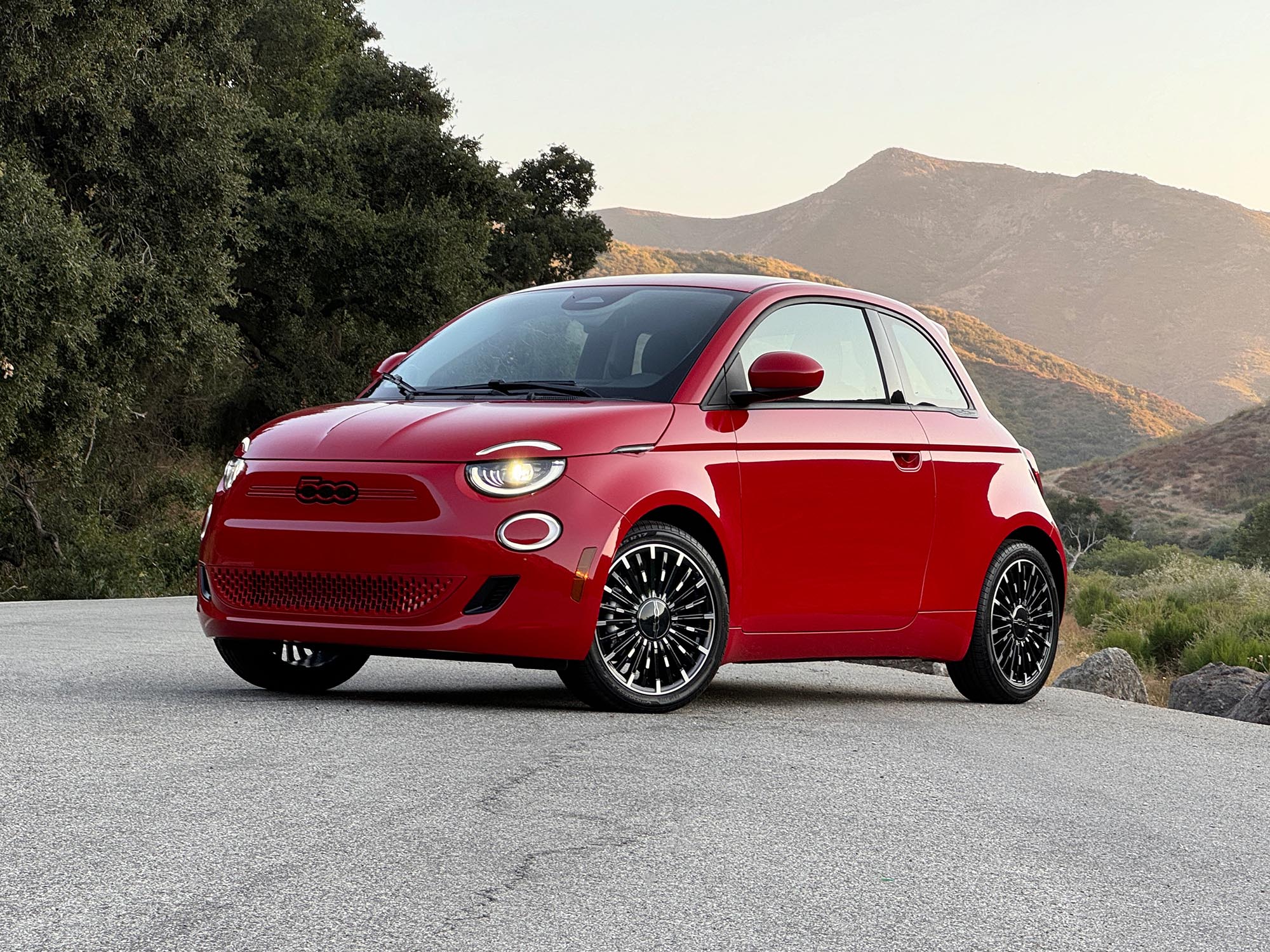 2024 Fiat 500e parked on a road at sunset with trees and mountains in the background