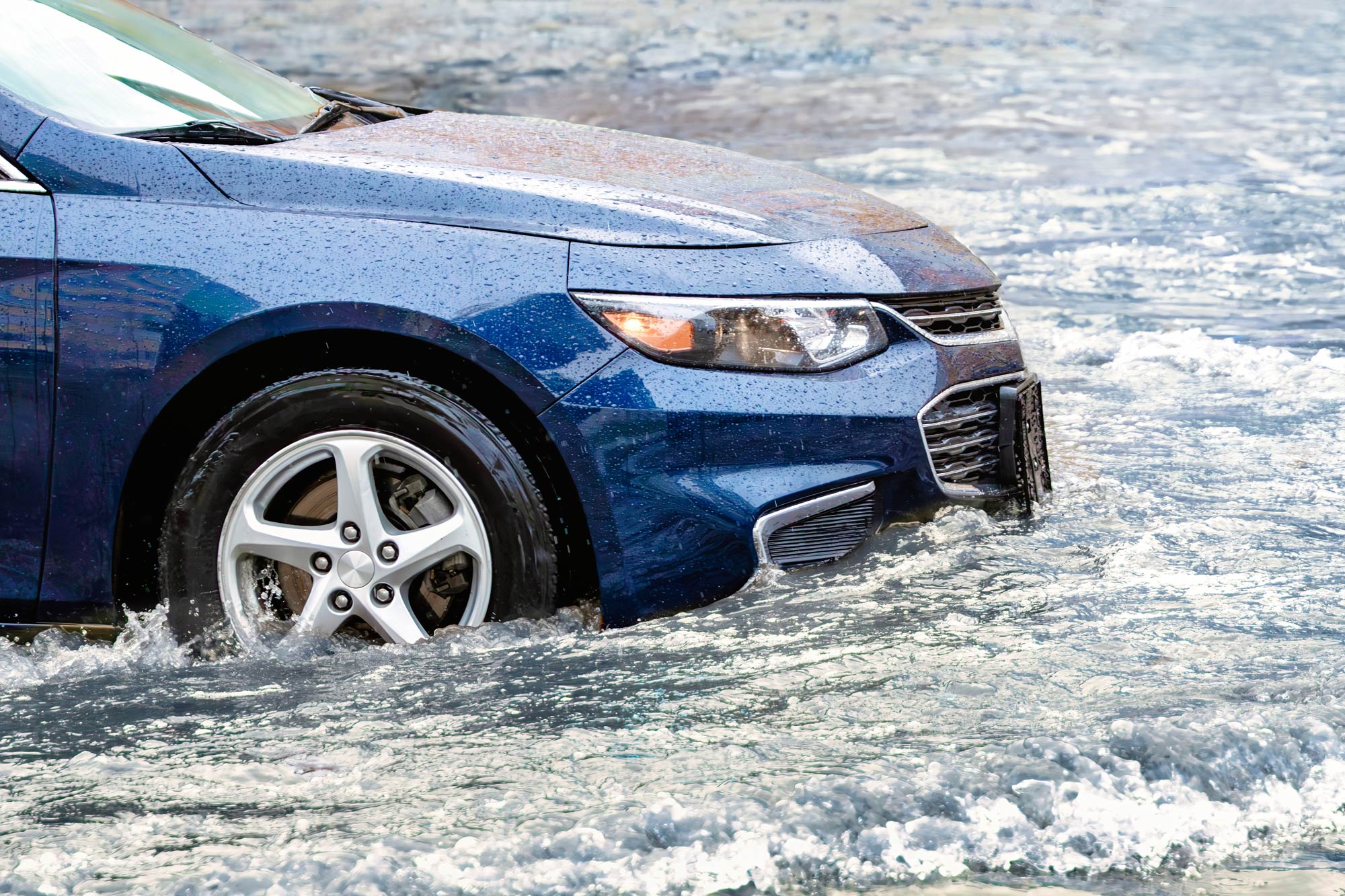 Blue car drives through a flood in the pouring rain