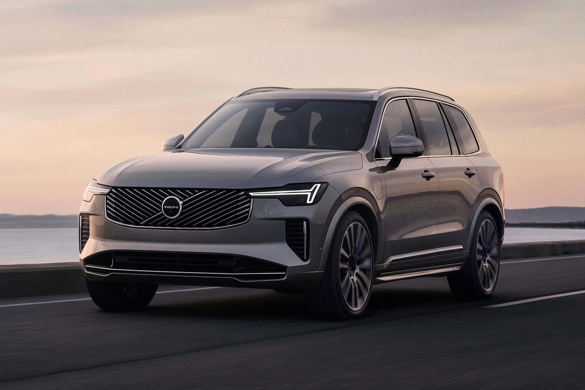 Front left view of a 2025 Volvo XC90 driving on highway in front of water.