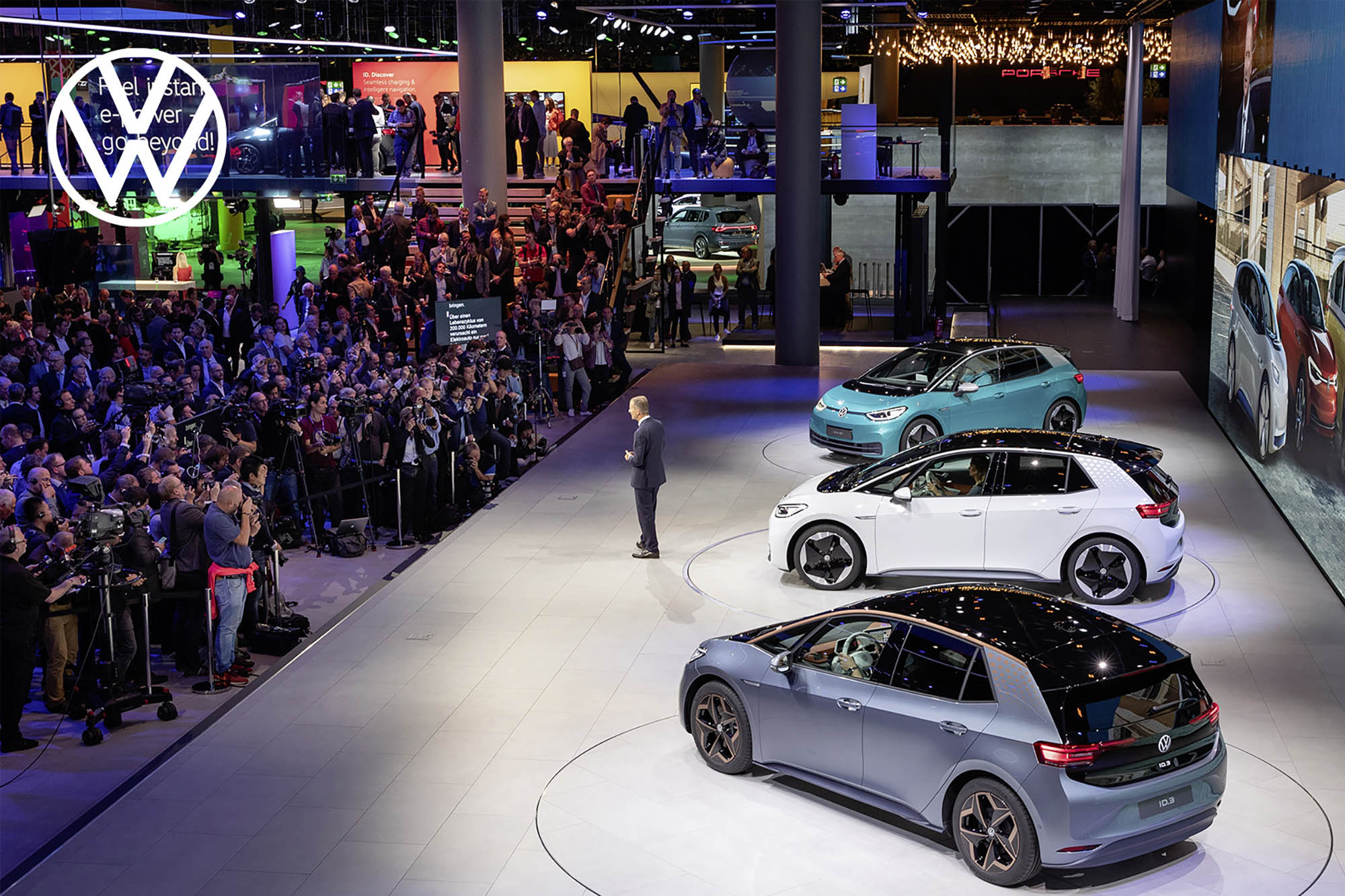 Volkswagen presentation with three vehicles on stage and a person giving a talk to an audience.