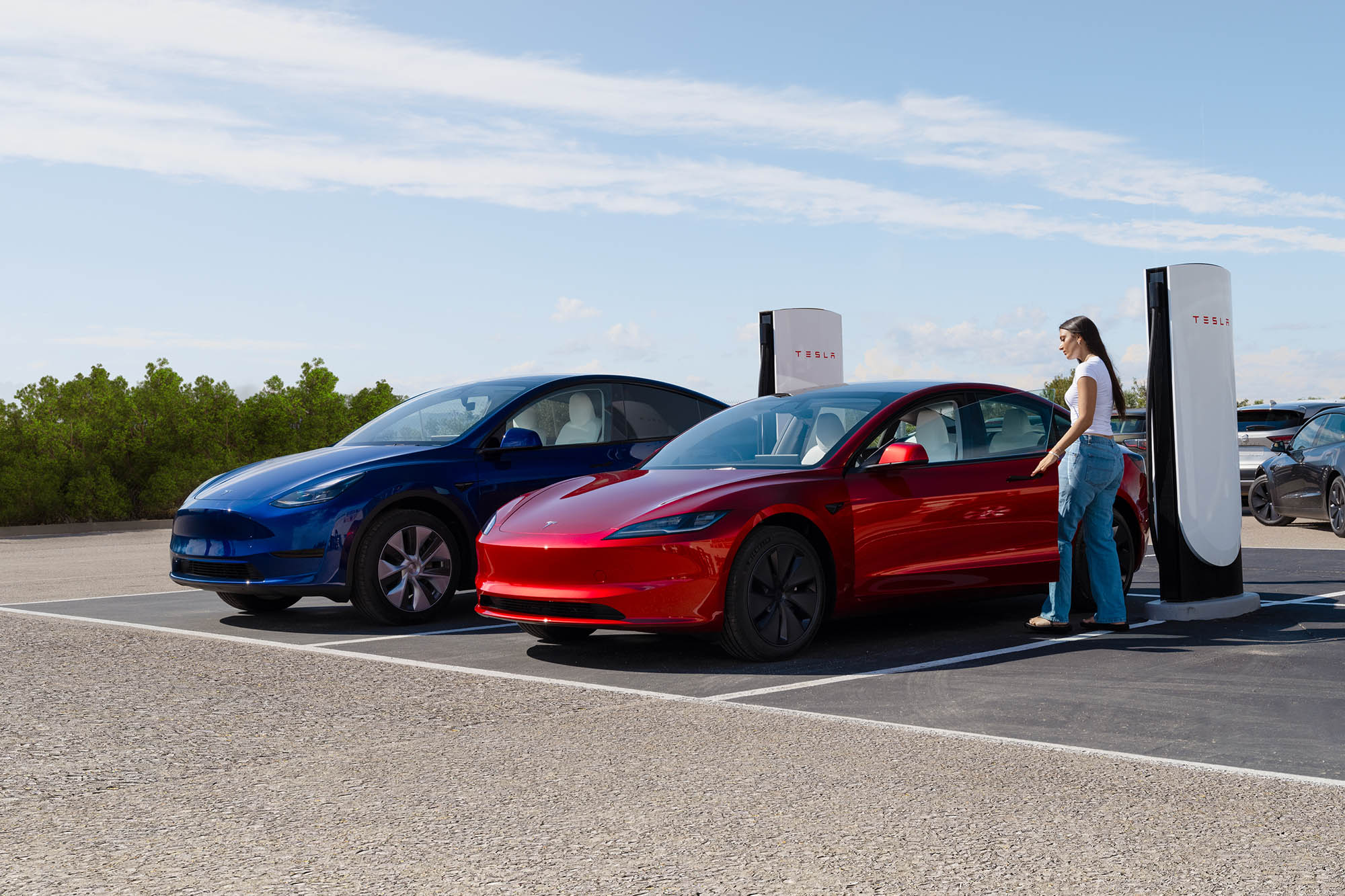 Person opening the driver's door of a red Tesla Model 3 parked at a Tesla V4 Supercharging station.