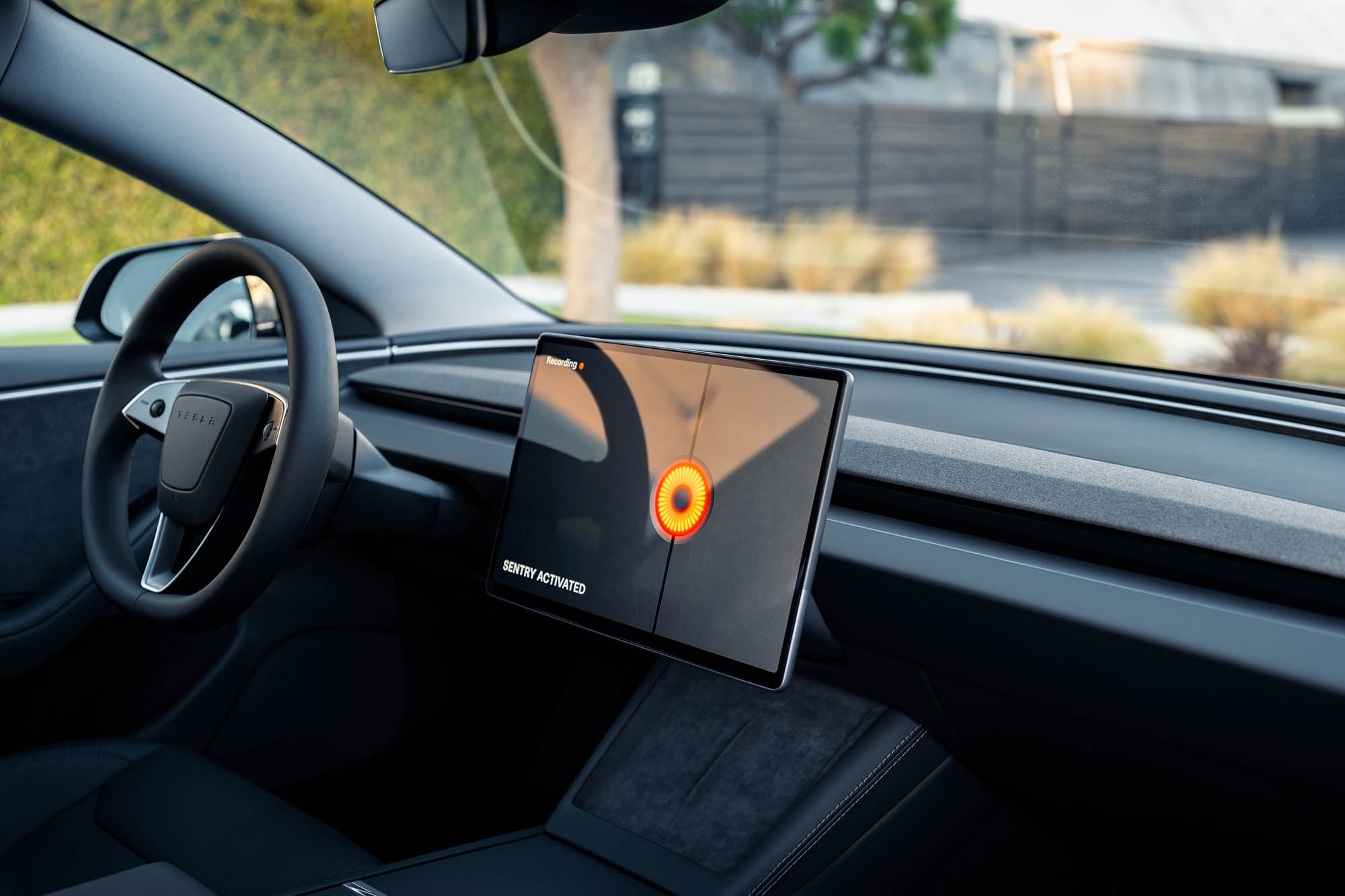 Inside of a Tesla Model 3 with Sentry Mode engaged and an orange circle on the infotainment screen.