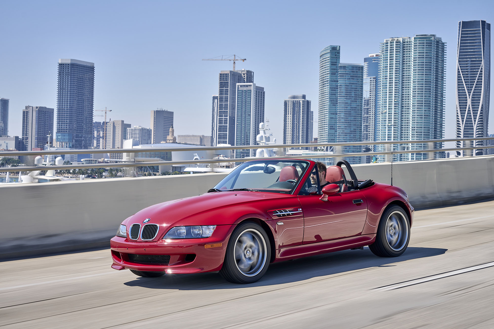 1999 BMW Z3 M Roadster in red driving on a bridge.