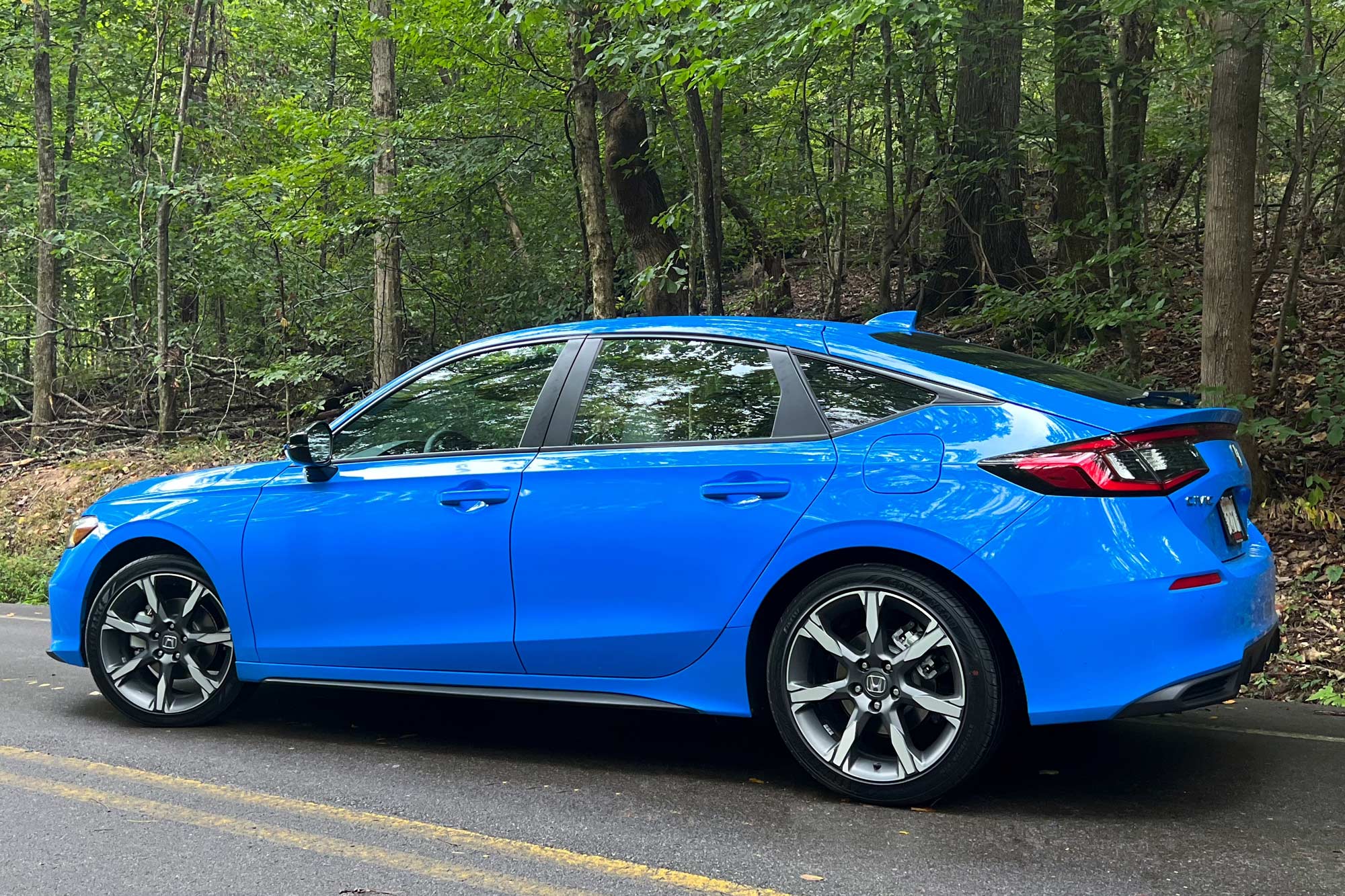 Side of a 2025 Honda Civic Sport Touring Hybrid hatchback in Boost Blue