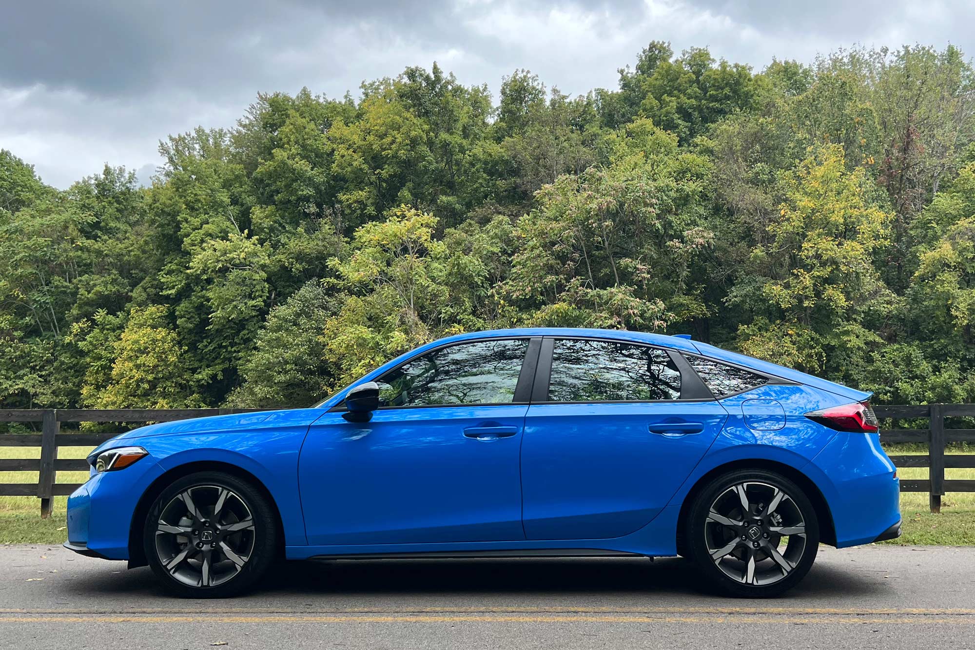 Side of a 2025 Honda Civic Sport Touring Hybrid hatchback in Boost Blue