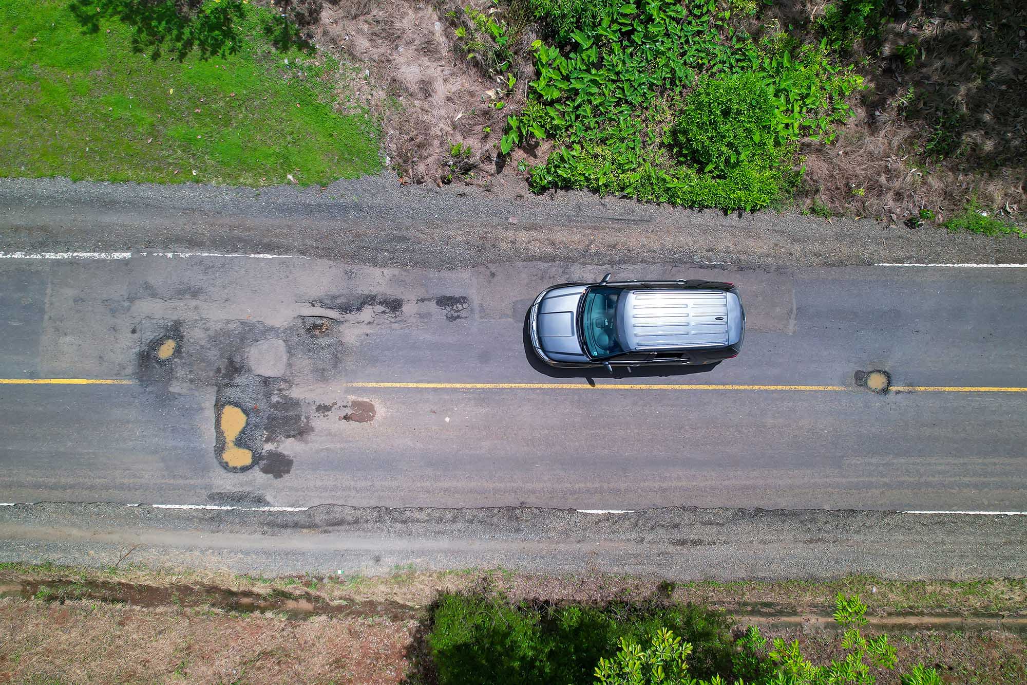 Aerial view of silver vehicle on pavement with potholes ahead.