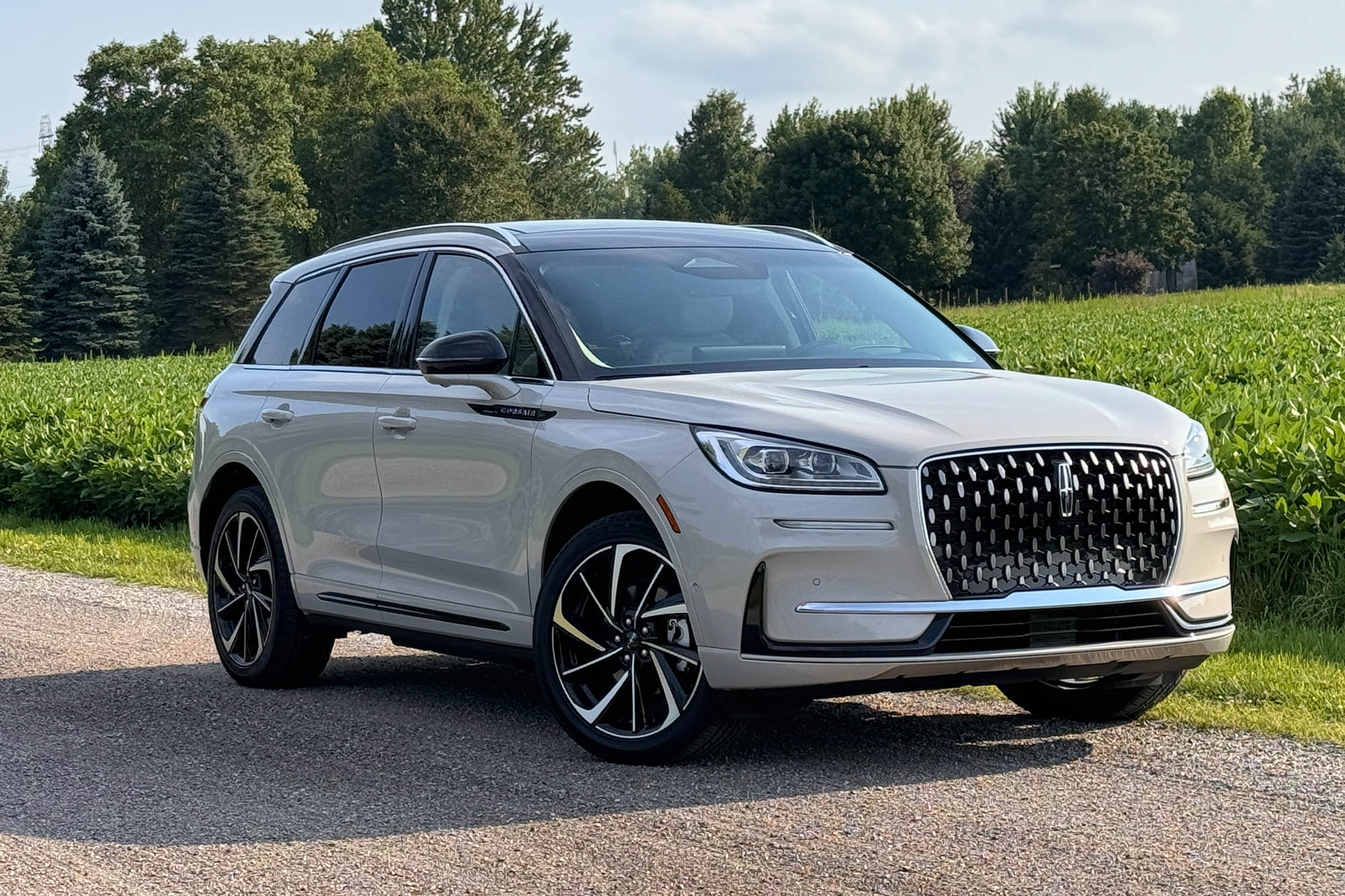 2024 Lincoln Corsair Grand Touring in Ceramic parked on a dirt road with a field and trees in the background.