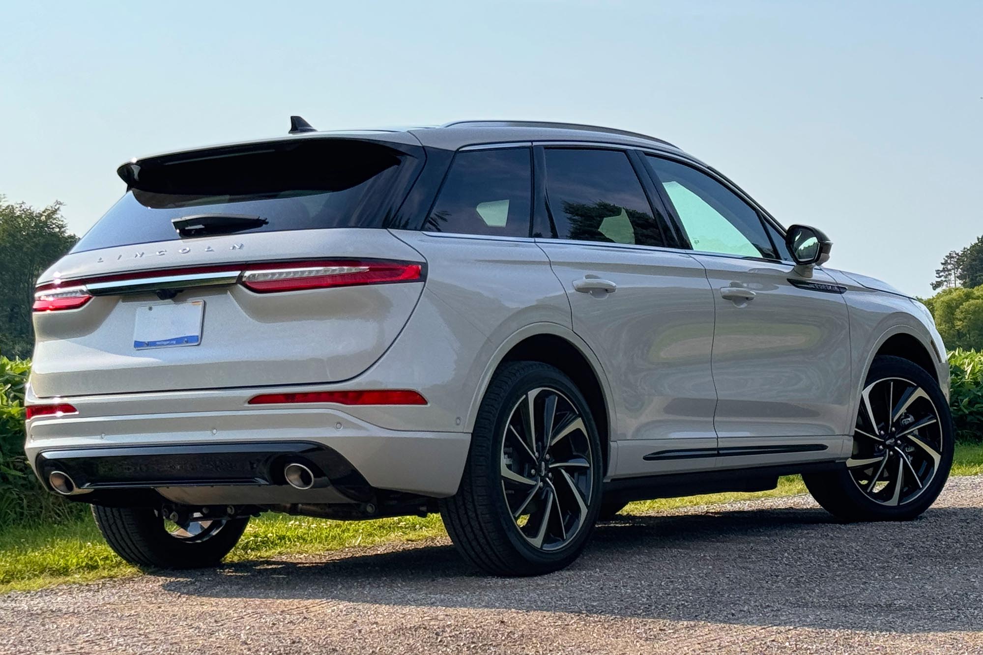 2024 Lincoln Corsair Grand Touring in Ceramic parked on a dirt road with a field and trees in the background.