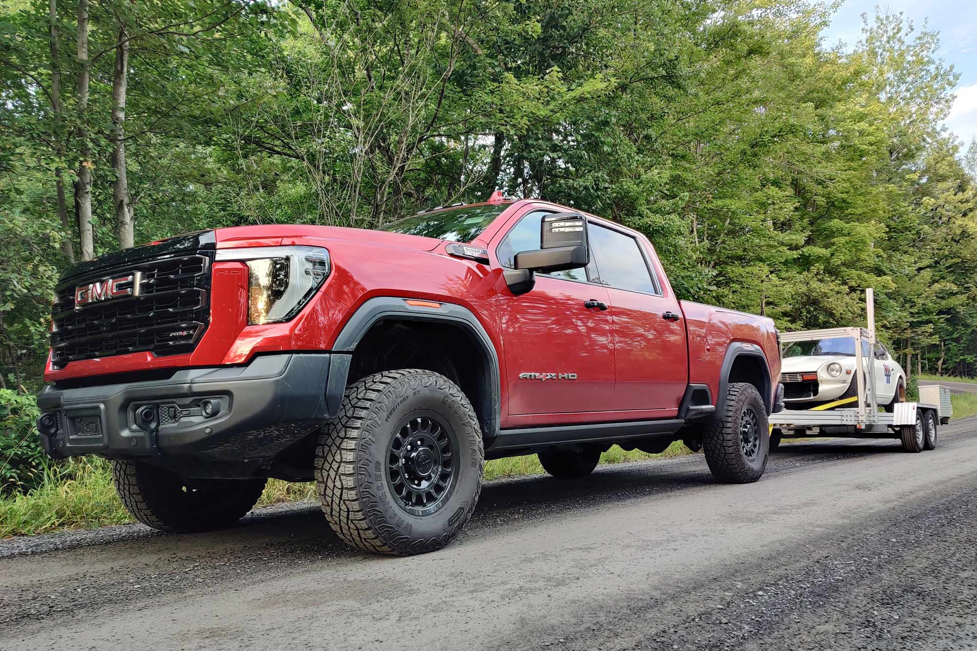 2024 GMC Sierra 2500HD AT4X AEV in Volcanic Red towing a white Datsun 240Z race car on a trailer