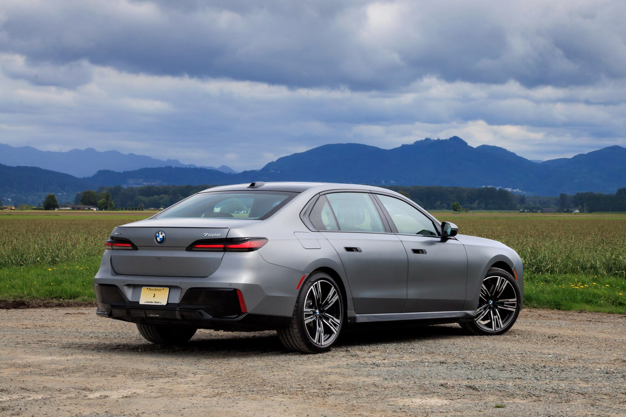 2024 BMW 750e plug-in hybrid in Frozen Pure Grey Metallic, rear view, with mountains in the background