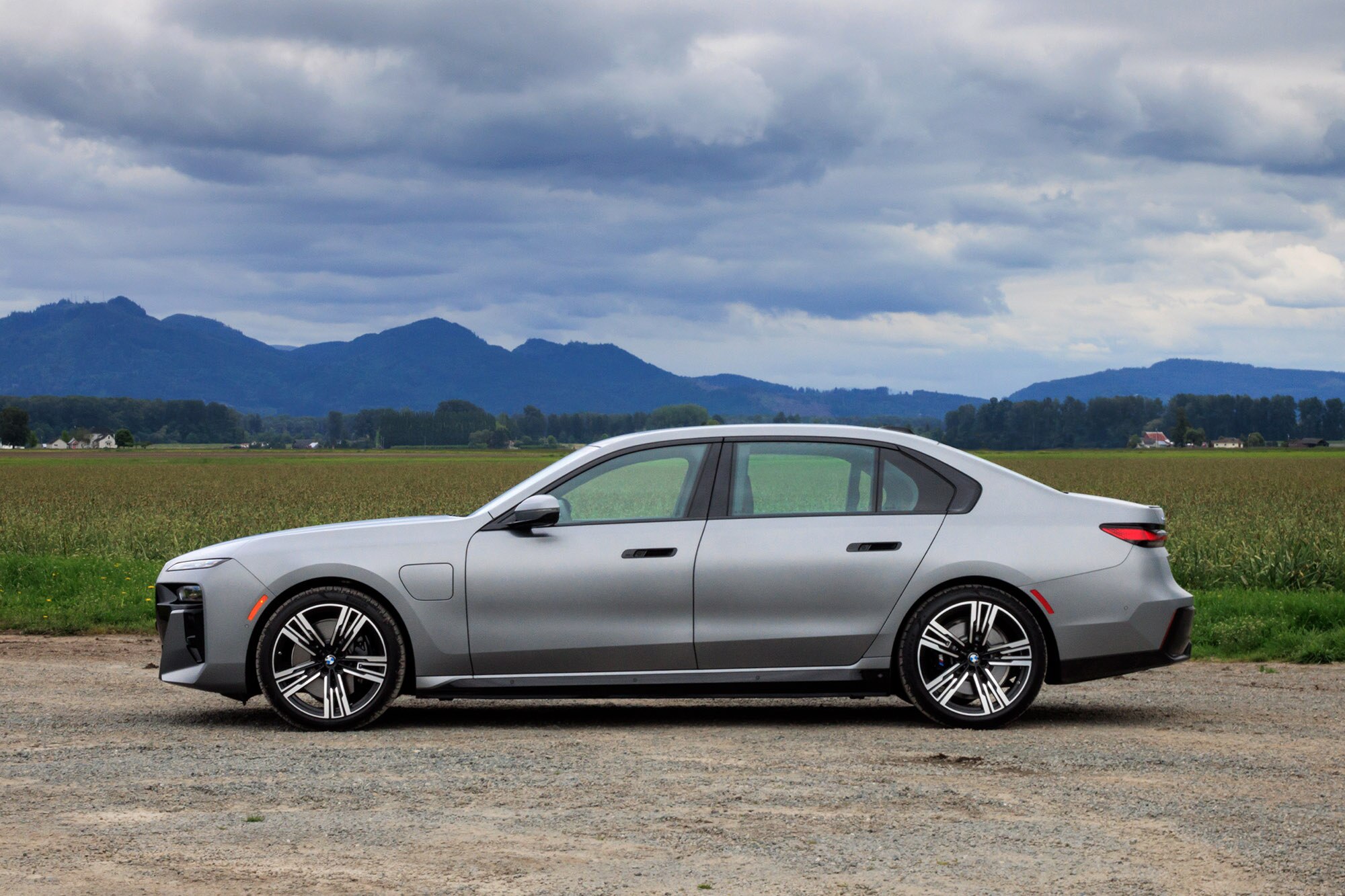 2024 BMW 750e plug-in hybrid in Frozen Pure Grey Metallic, side rear view with mountains in the background