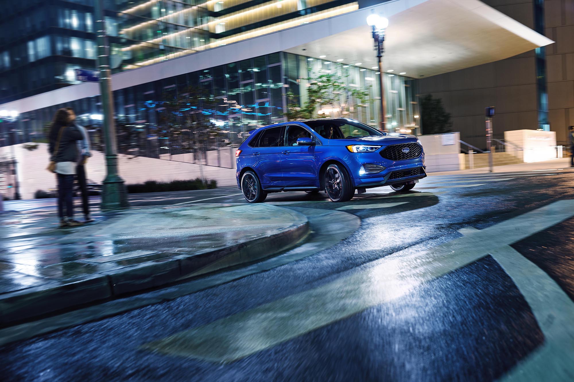 A blue Ford Edge driving in an urban environment at night.