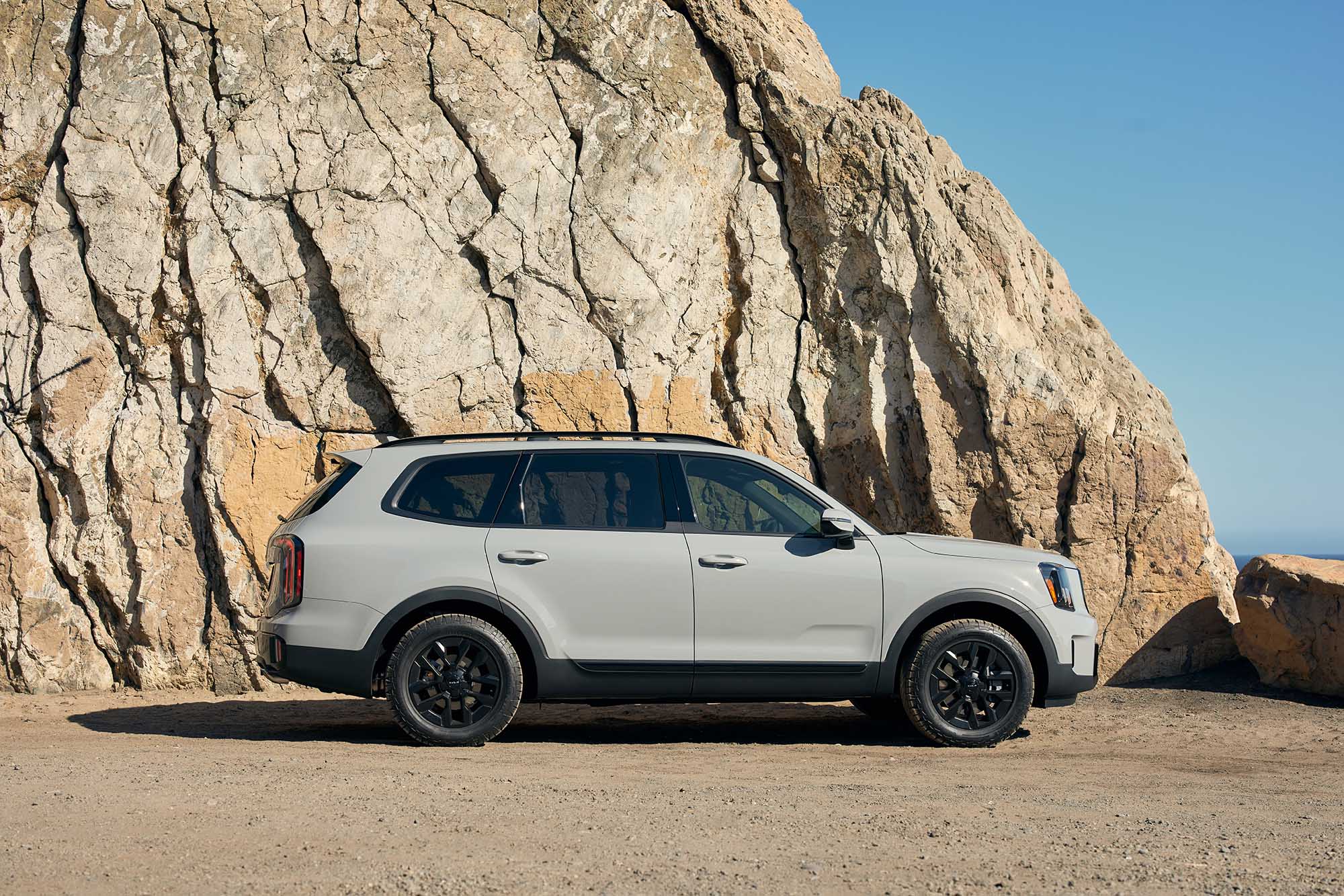 Light gray Kia Telluride parked next to a rock formation.