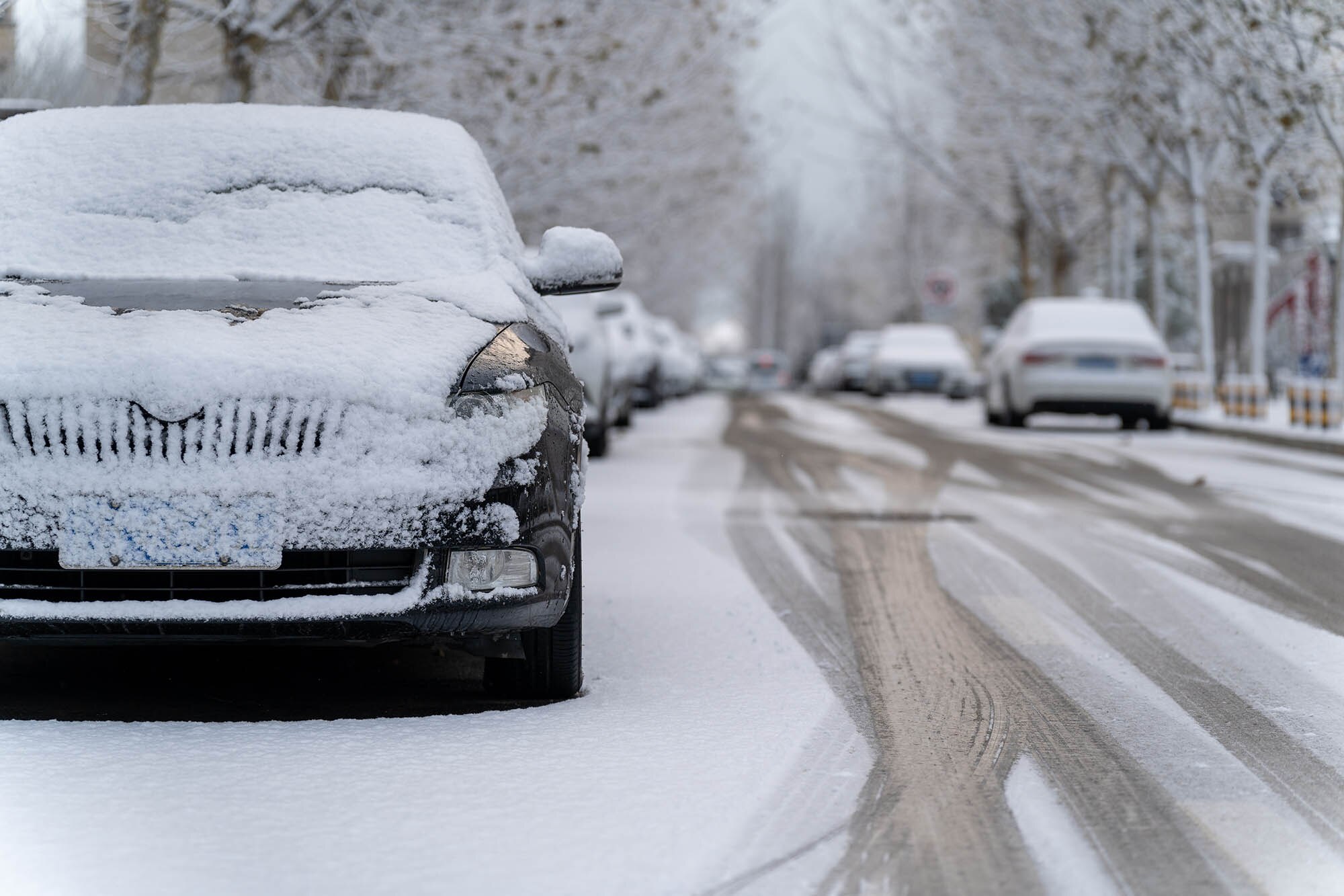 A black car with snow covering it parked on an icy street.