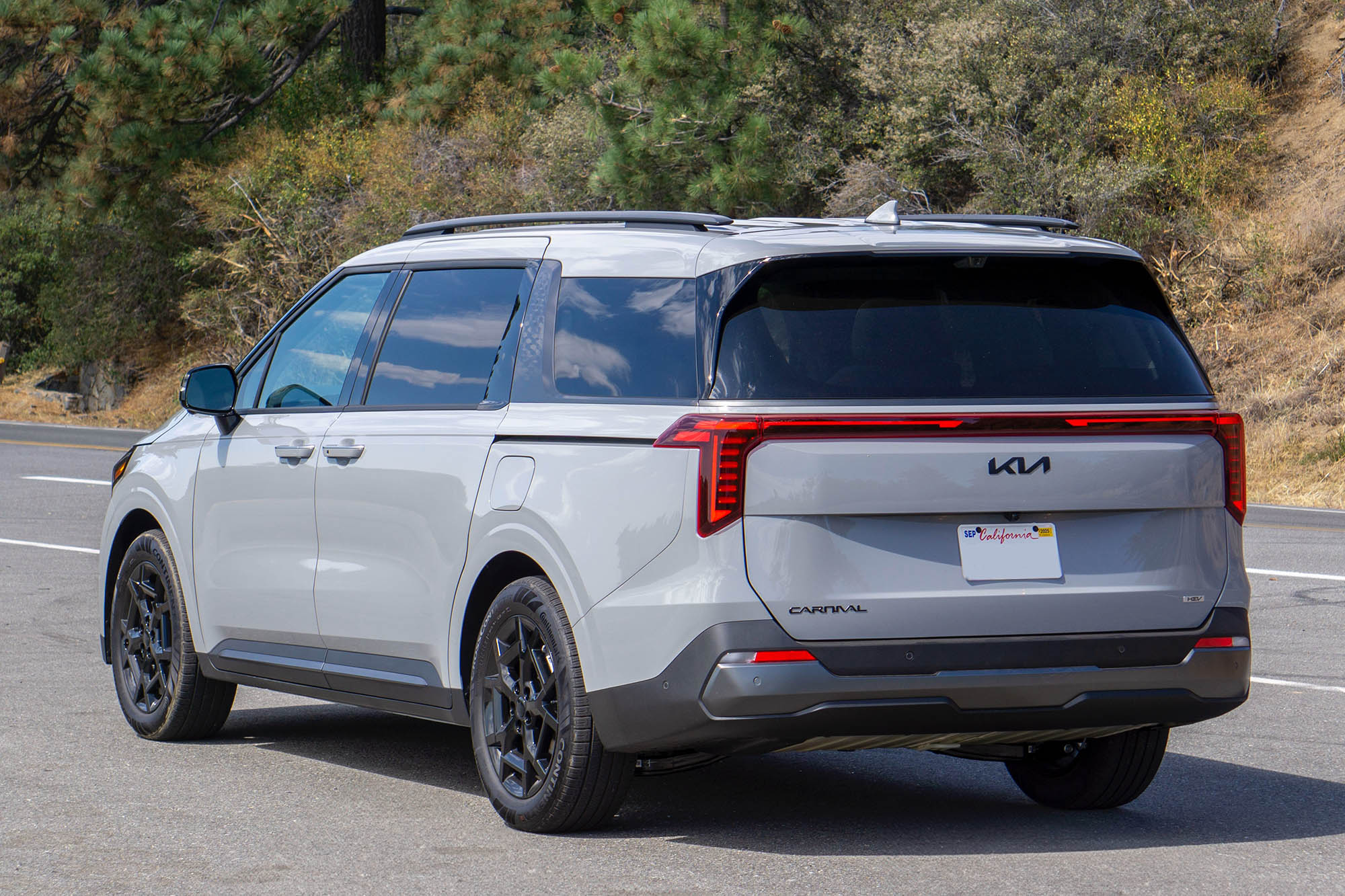 2025 Kia Carnival Hybrid SX Prestige in Ceramic Silver with bushes and trees in the background.