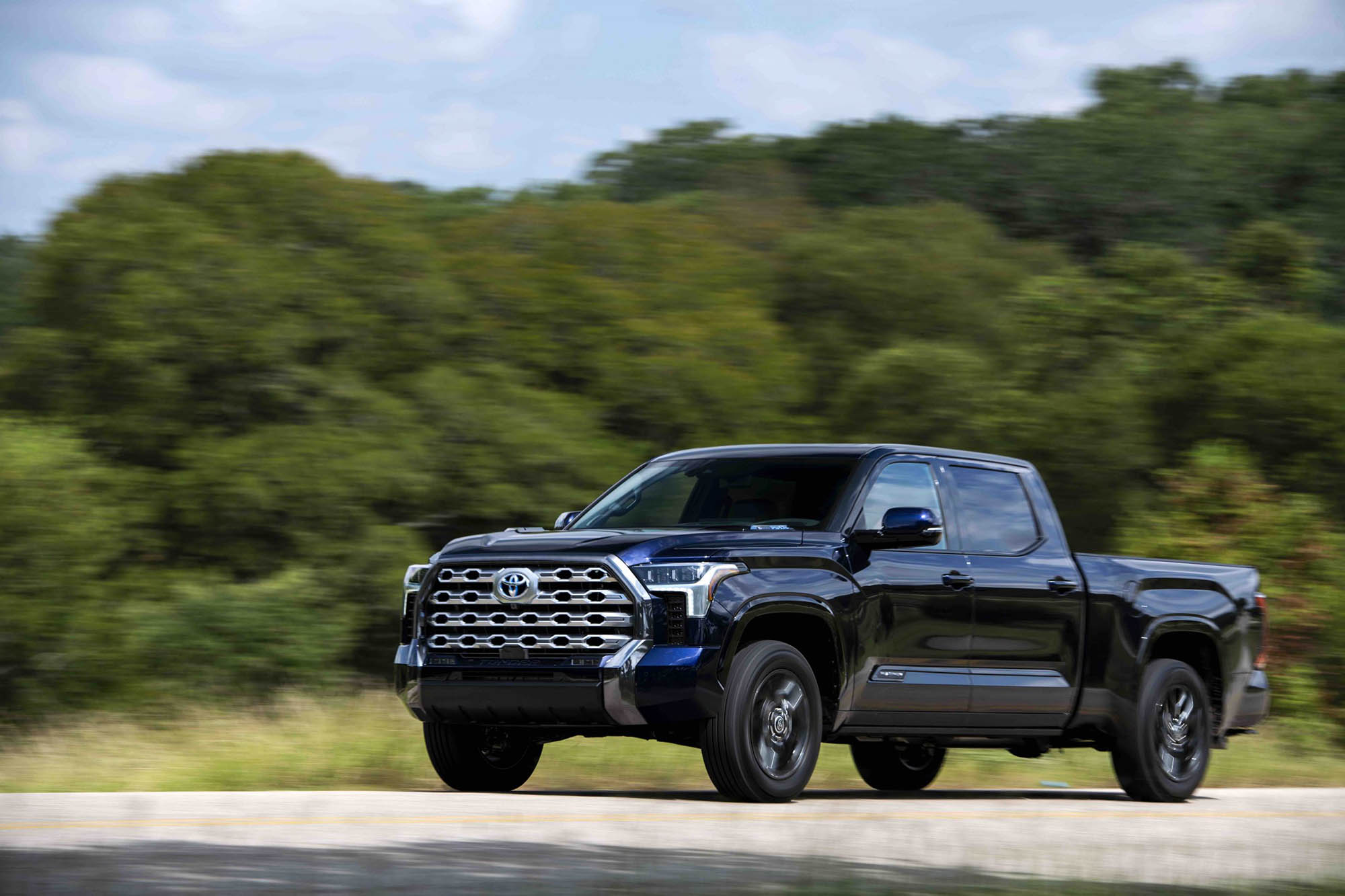 Dark blue Toyota Tundra driving on a paved road with trees in the background.