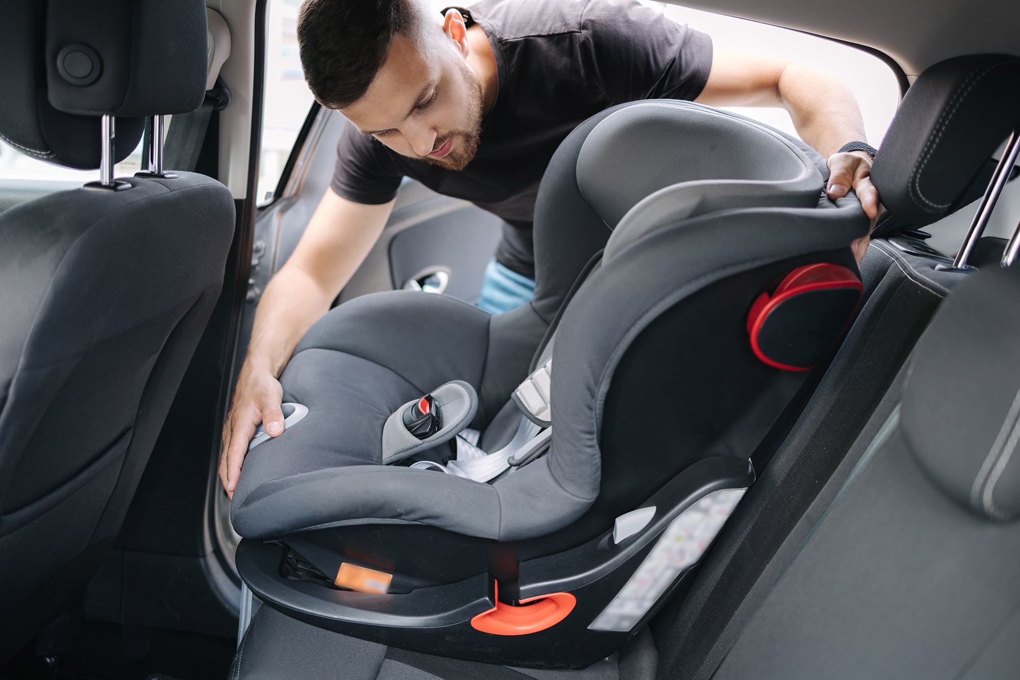 Person installs a forward-facing child car seat in the back seat of a vehicle.