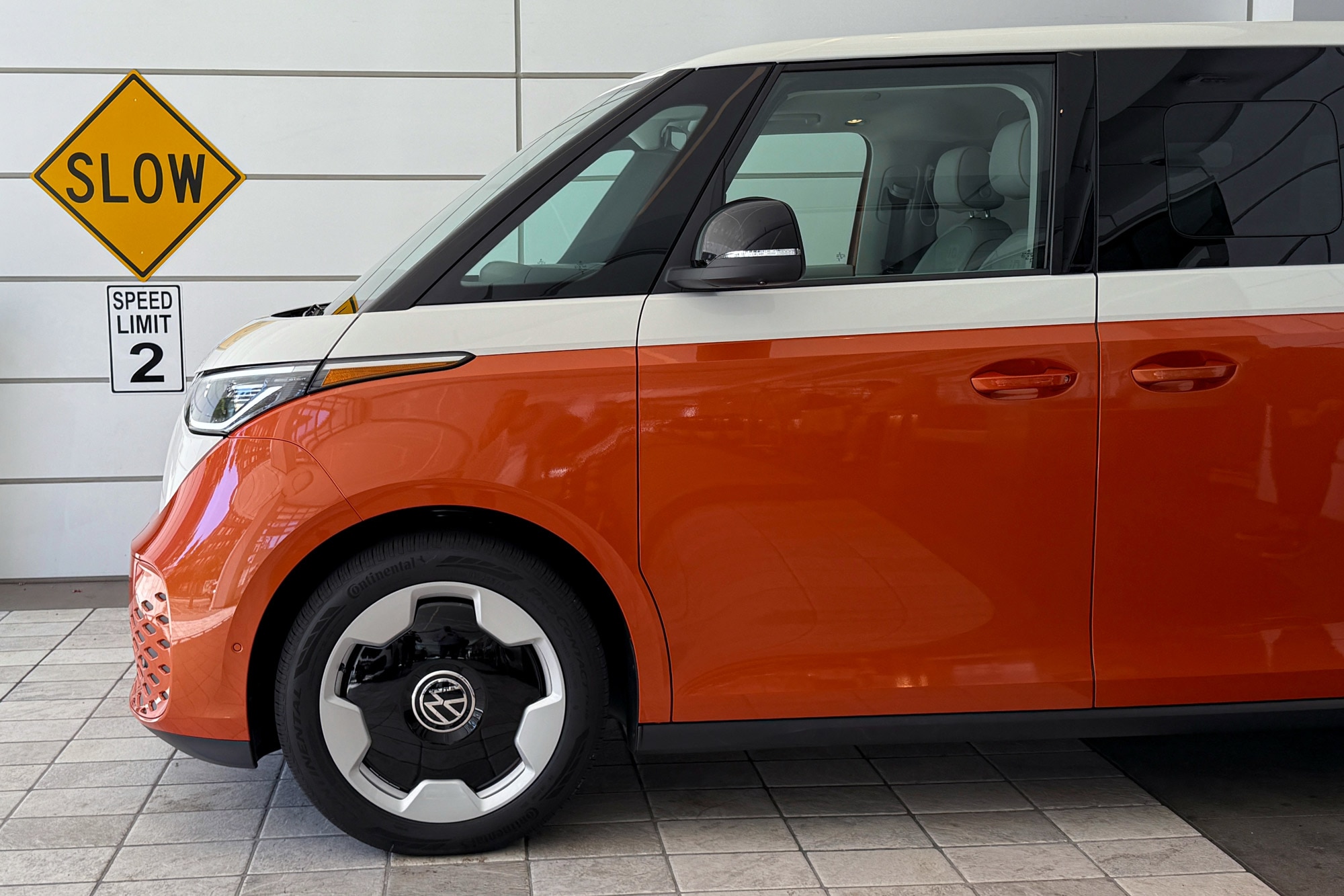 2025 Volkswagen ID. Buzz Pro S Plus in Candy White over Energetic Orange, with a Slow sign in the background.