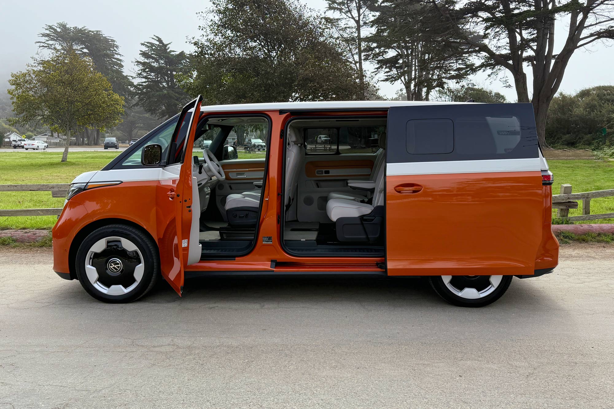 2025 Volkswagen ID. Buzz Pro S Plus in Candy White over Energetic Orange, with a park and trees in the background.