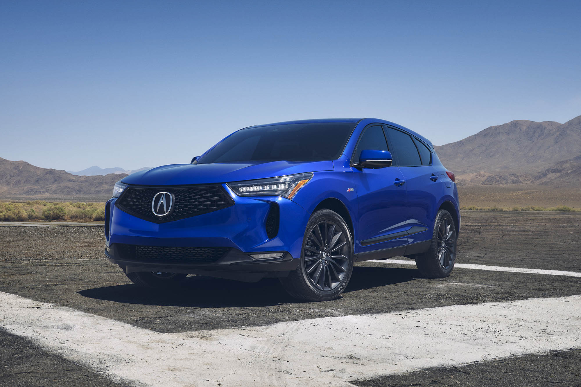 Blue Acura RDX parked on pavement with mountains in the background.