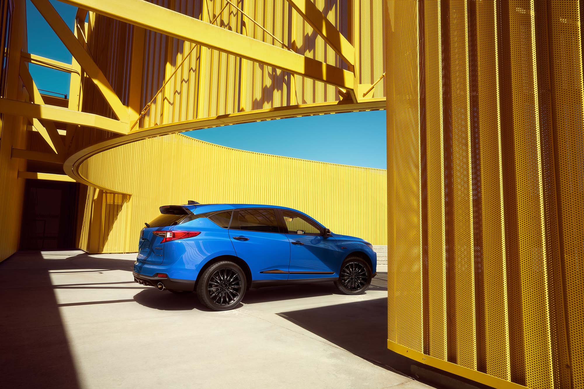 Blue Acura RDX parked beneath a semicircle of yellow mesh metal.