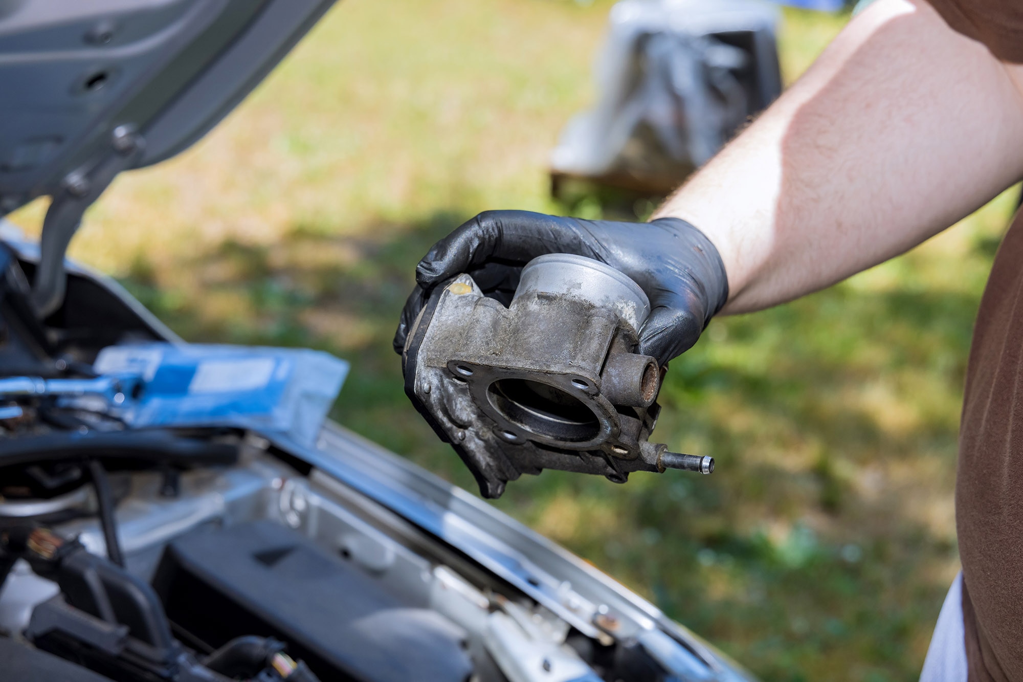 A mechanic holding a throttle body over an engine bay