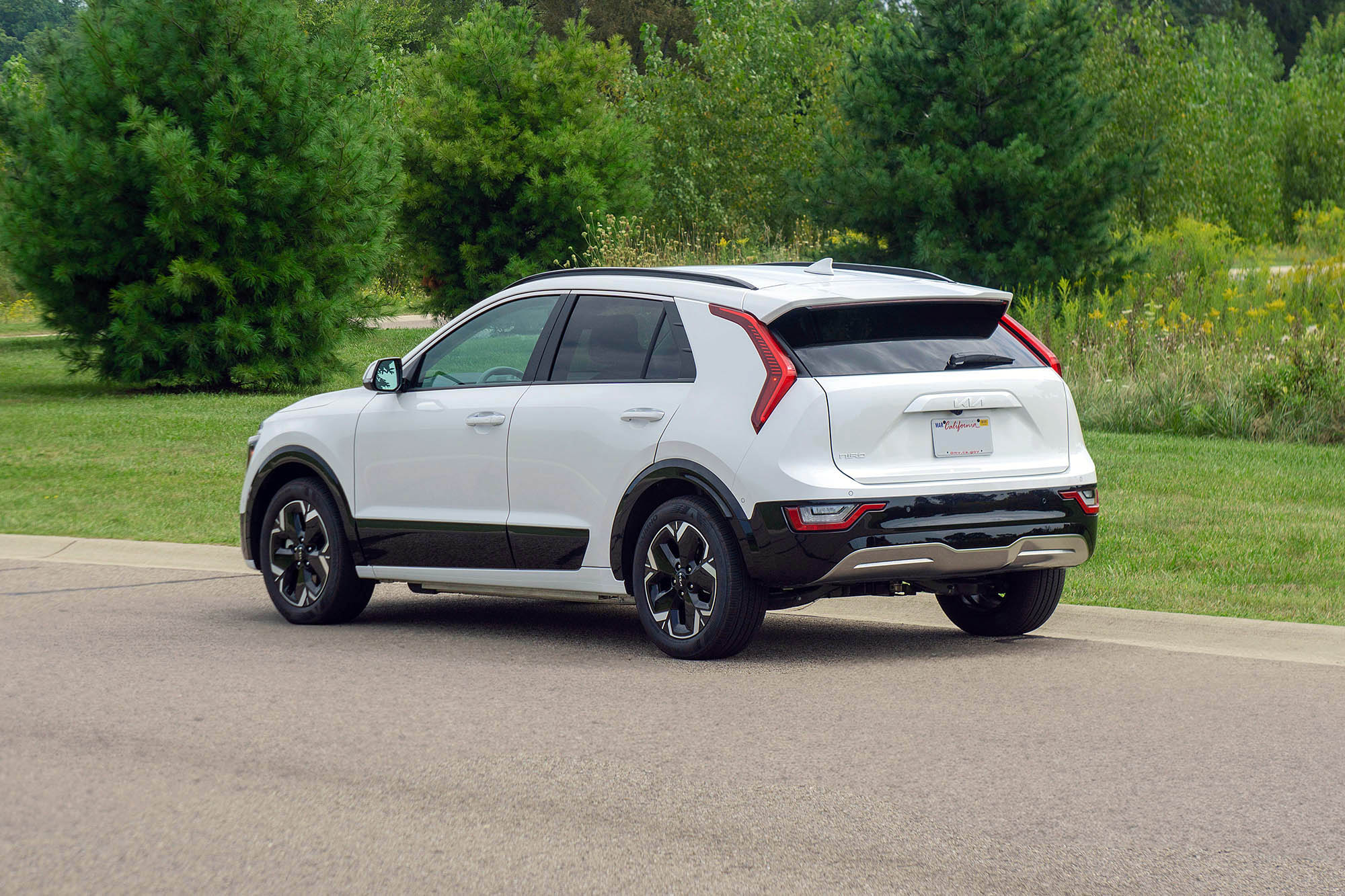 2024 Kia Niro EV Wave in Snow White Pearl, rear view with grass and trees in the background