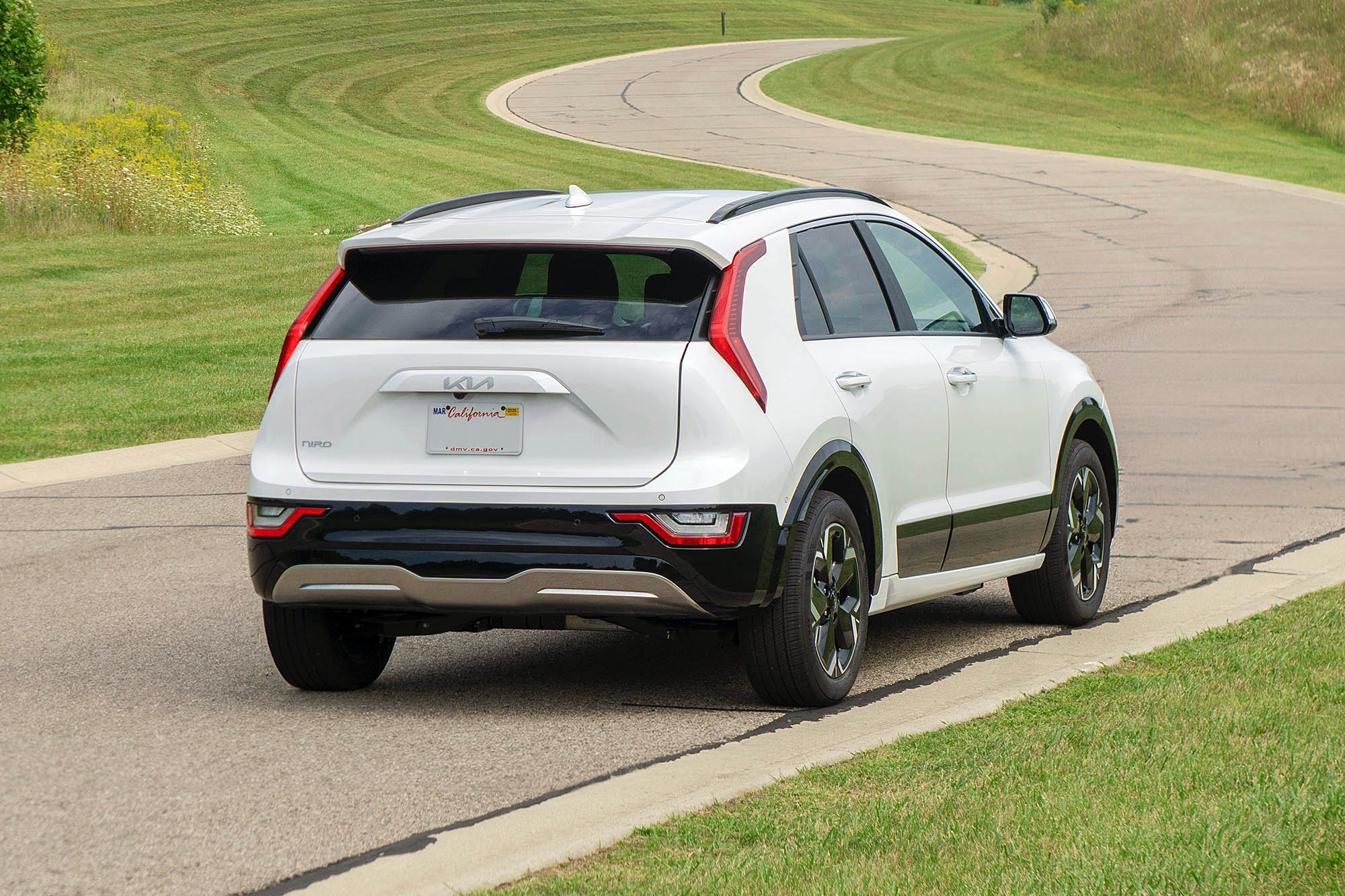 2024 Kia Niro EV Wave in Snow White Pearl, rear view with grass and a winding road in the background