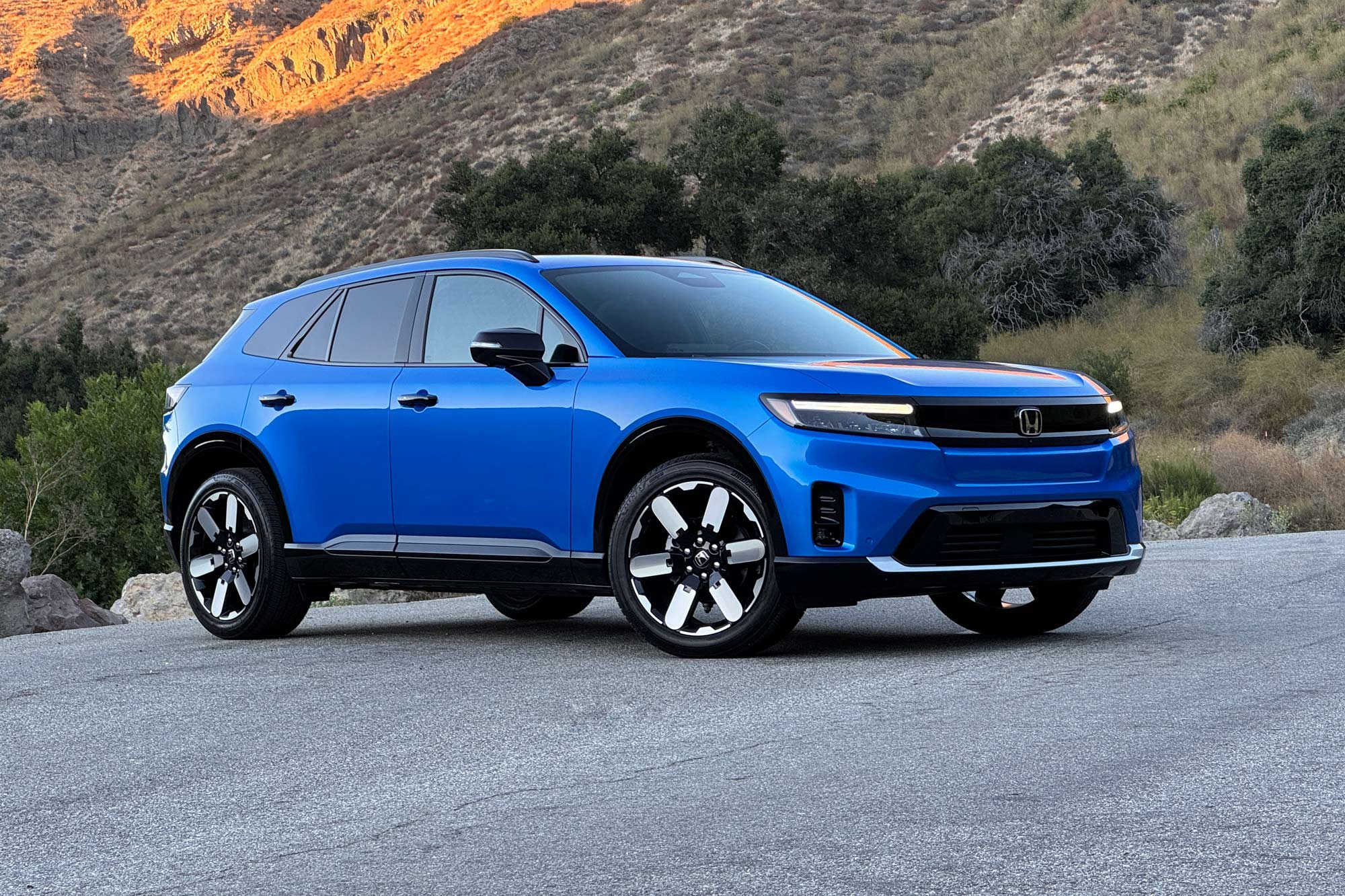 2024 Honda Prologue Elite in Pacific Blue with a brush-covered hill in the background.